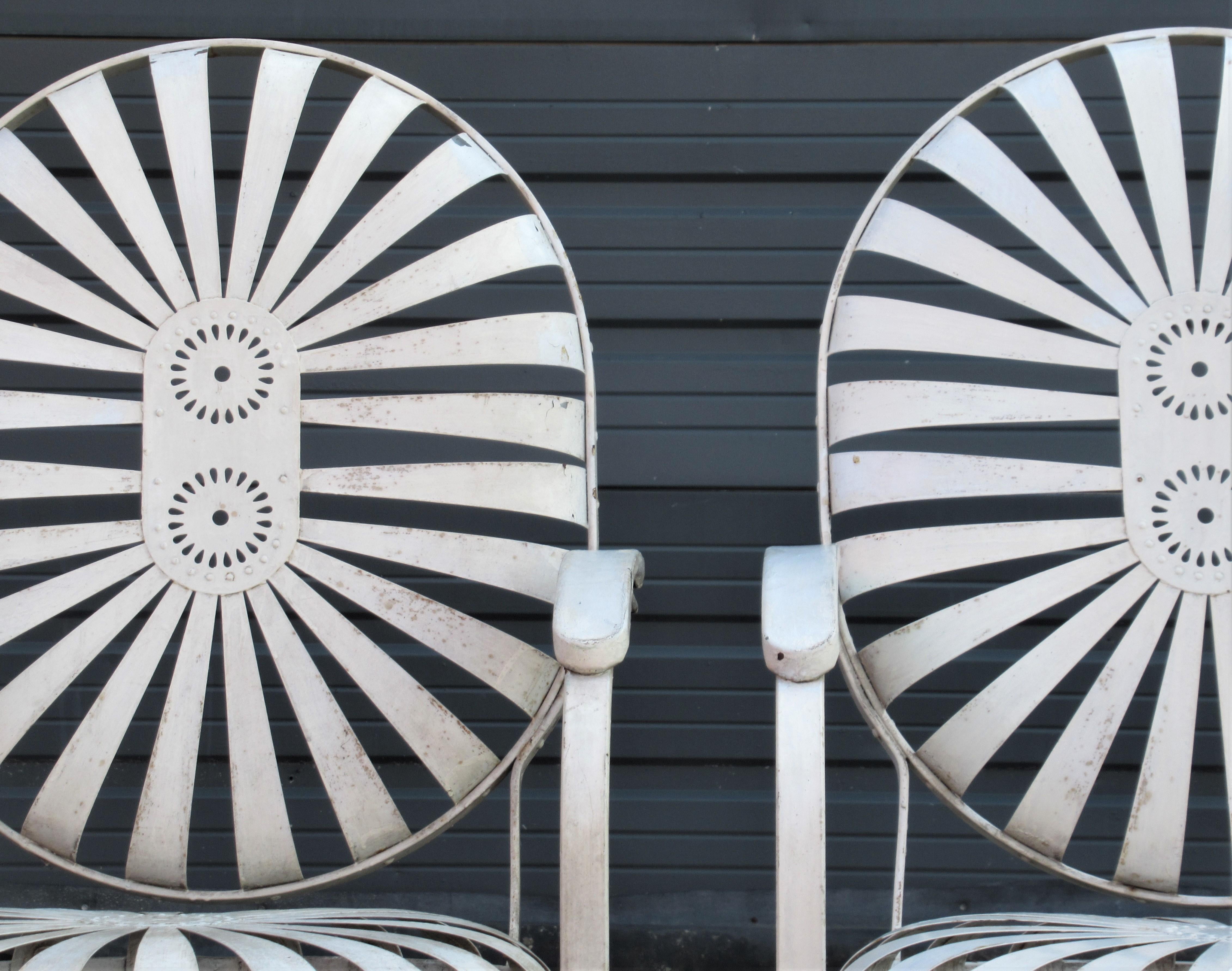 A matching set of four riveted steel spring sunburst double pinwheel design garden chairs with rocking cantilever legs and large raised armrests in overall original cream white satin painted surface. A hard to find oversize set of four by Francois