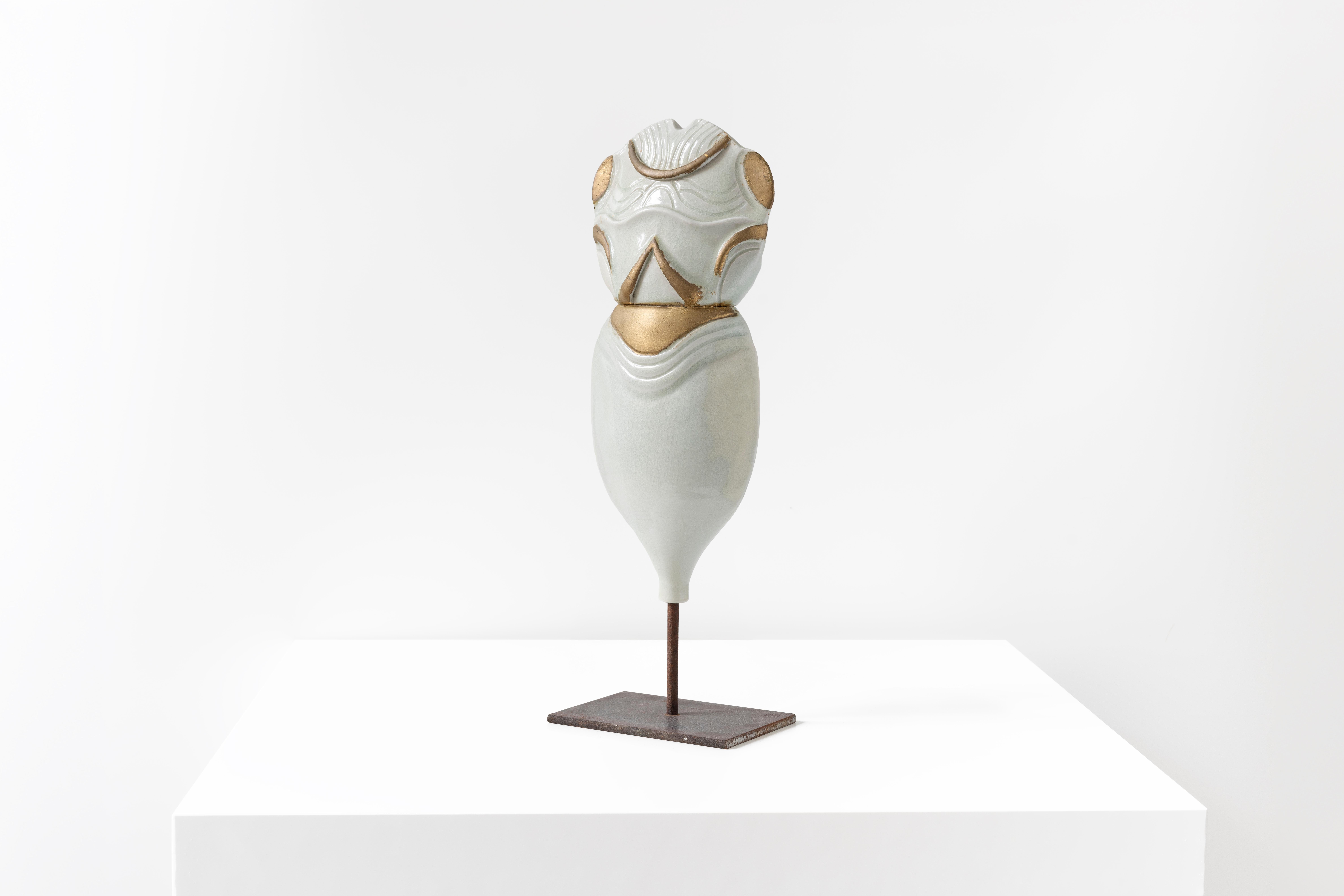 Este elegante tótem, diseñado por François Gueneau, tiene una forma suave y grácil hecha de porcelana. La parte superior muestra una forma abstracta con aspecto de torso, adornada con elegantes detalles dorados y bajorrelieves que realzan su