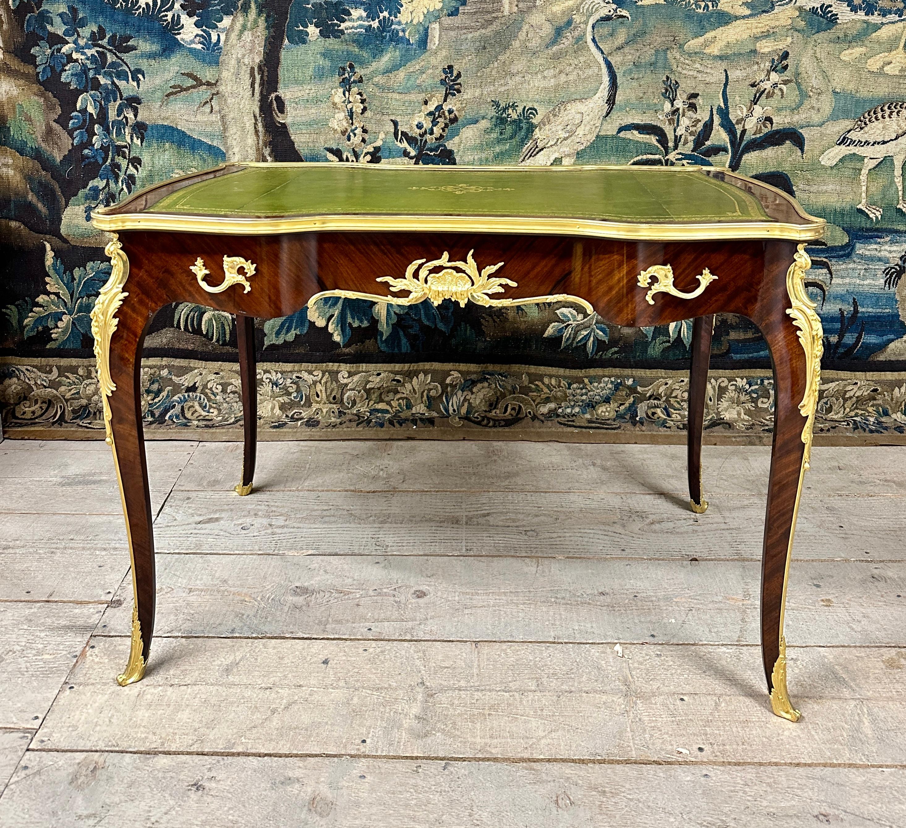 Louis XV style flat desk richly decorated with chiseled and gilded bronzes with in particular large shells on the front and back facade. It is mahogany veneer and has a top covered with green leather. It opens with a belt drawer closing with its