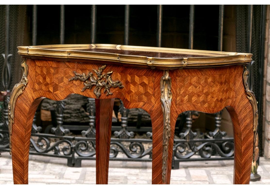 A parquetry inlaid side table, having a hinged top, opening to reveal a shaped and divided compartment within. The bronze trimmed cartouche formed top with cross banding intertwined with flowers and vines. The table is finished on all four sides