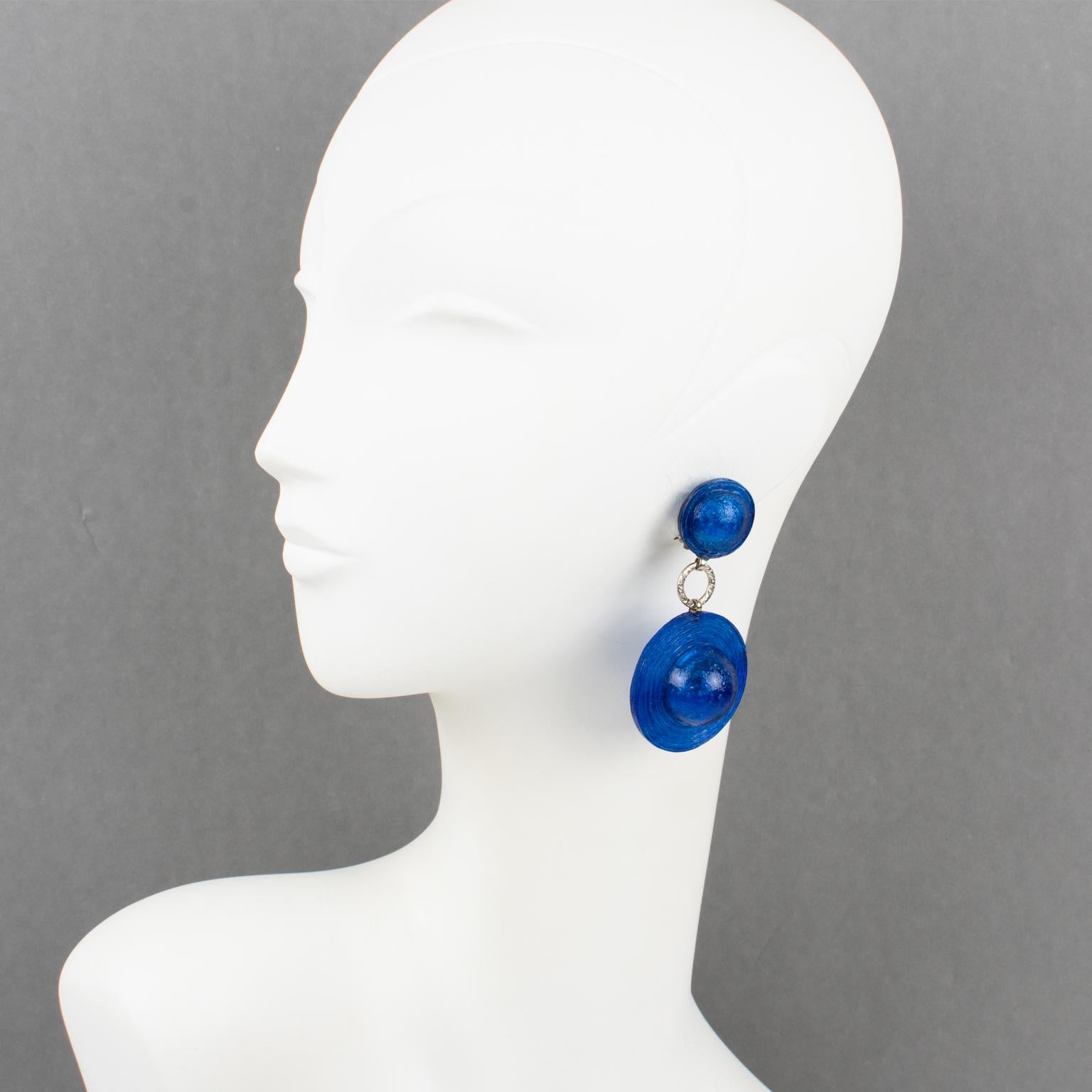 These lovely Francoise Montague Paris clip-on earrings, designed by Cilea Paris, feature an oversized dangle design in shiny translucent cobalt blue resin in a hat-like shape. The hardware and fastenings are in silvered metal. There is no visible