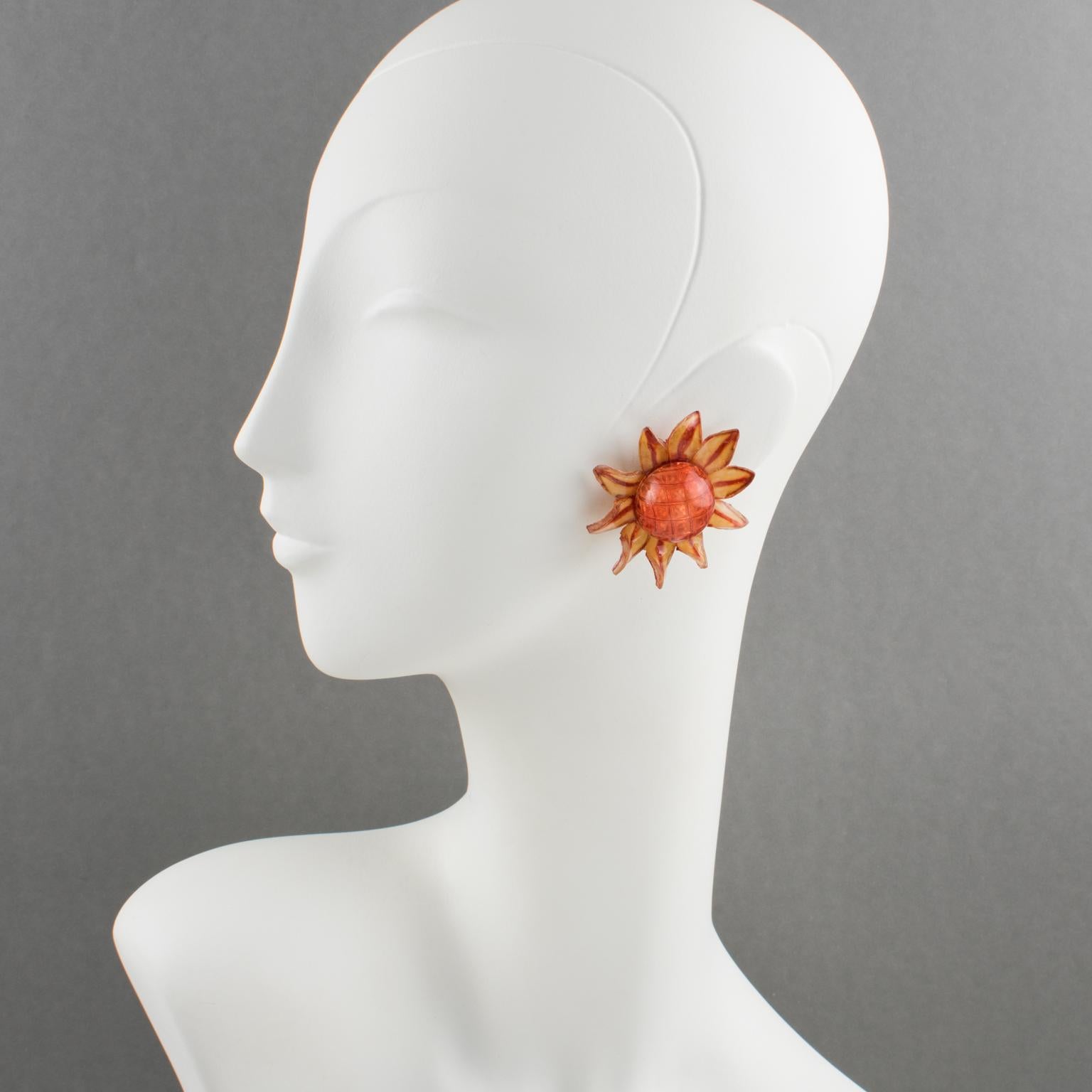 These elegant resin clip-on earrings were designed by French Jewelry artist Francoise Montague Paris and manufactured by Cilea. They feature a dimensional daisy flower shape with textured patterns in red, custard, and orange assorted colors. There