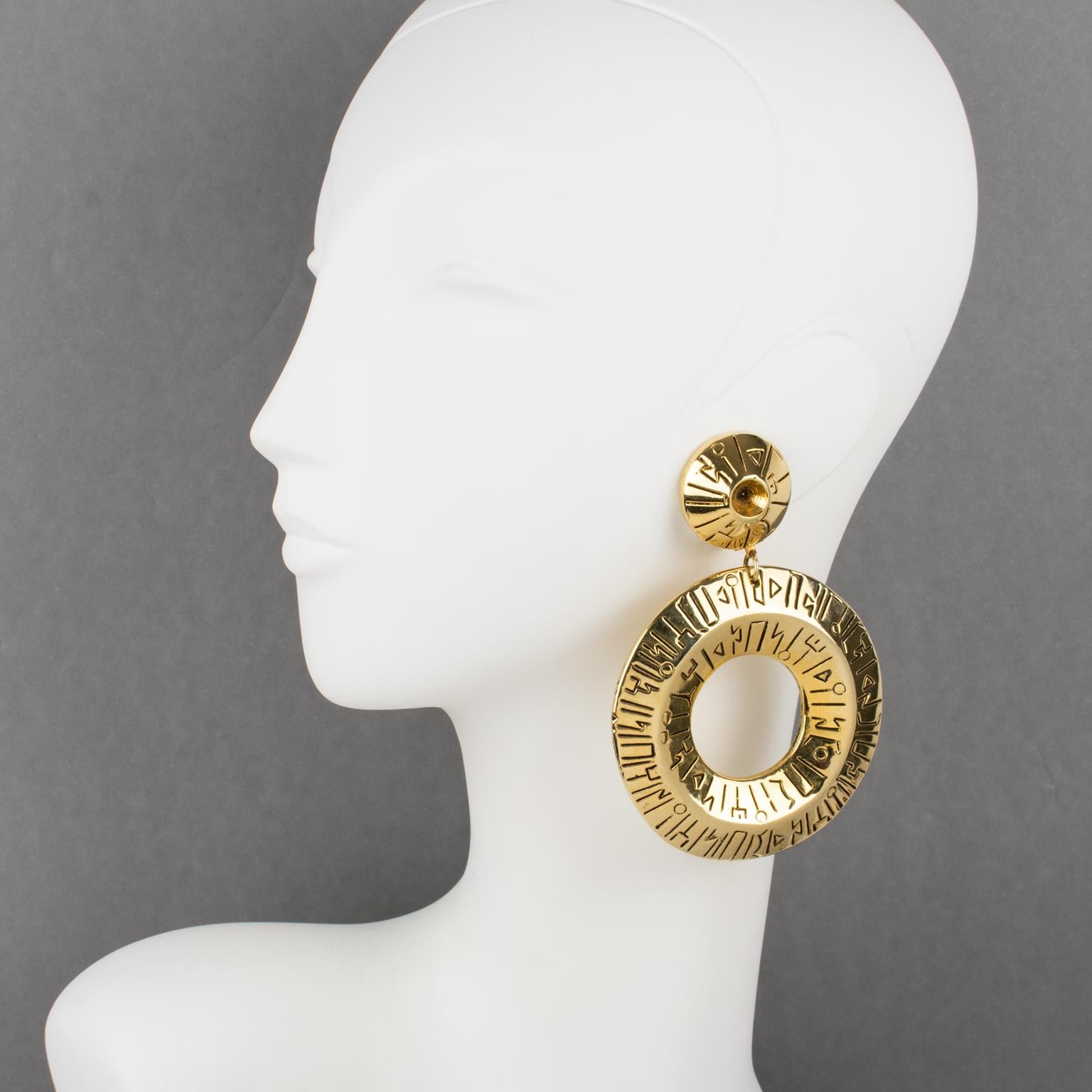 Stunning oversized Francoise Montague Paris resin clip-on earrings designed in the 1980s. 
A dangle shape features a massive gilt metal coating resin donut with ethnic carving. 
Shiny gold color with black contrast carved inscriptions. There is no