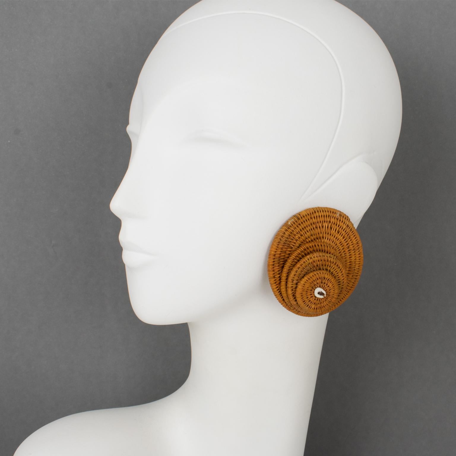These beautiful clip-on earrings made of wicker or rattan were created and crafted by French designer Francoise Montague during the 1960s. The dimensional shape boasts wicker or rattan woven work with a textured pattern. The four graduated disks are