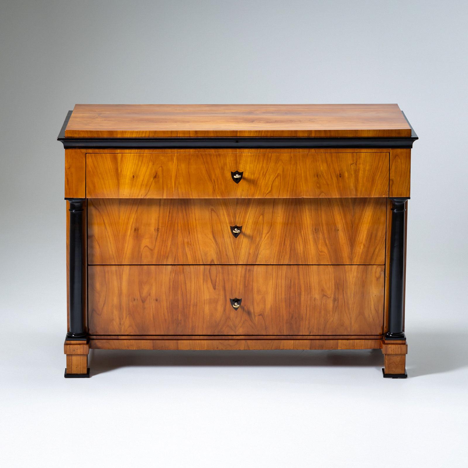 Elegante Biedermeier-Kommode mit drei Schubladen, hergestellt um 1820. Die obere Schublade wird von ebonisierten Vollsäulen an den Seiten eingerahmt, die dem Möbelstück eine markante Struktur verleihen. Die quadratischen Beine und die Tischplatte