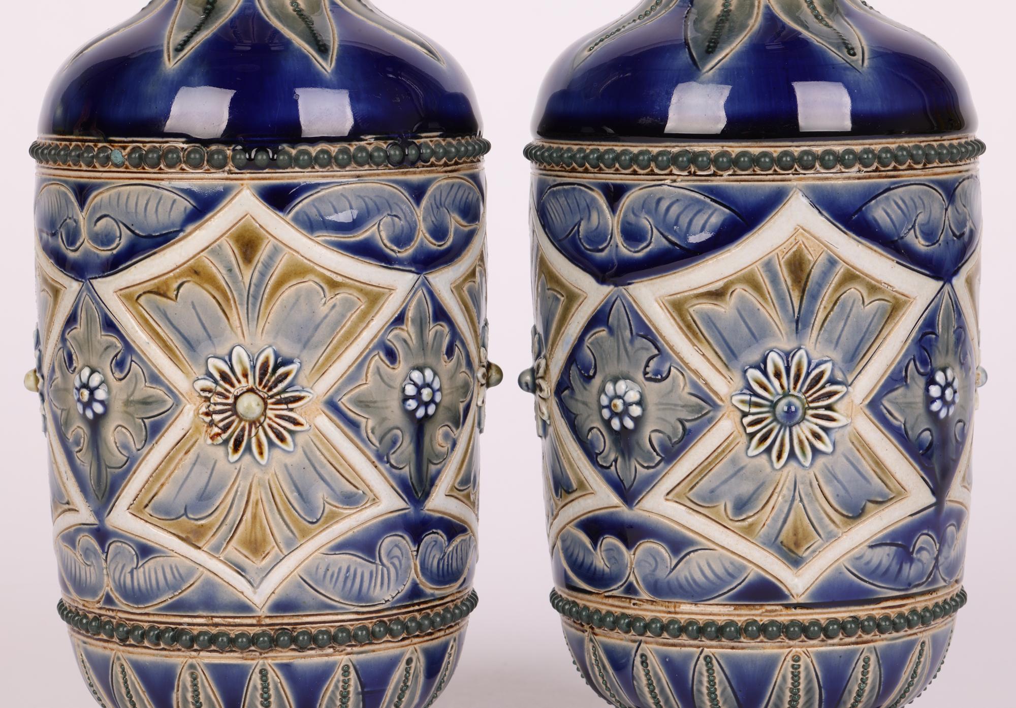 A stylish and decorative pair Aesthetic Movement Doulton Lambeth stoneware vases decorated with stylized floral designs by renowned artist Frank A Butler and dated 1882. The bottle shaped vases stand on a narrow round pedestal foot with cylindrical