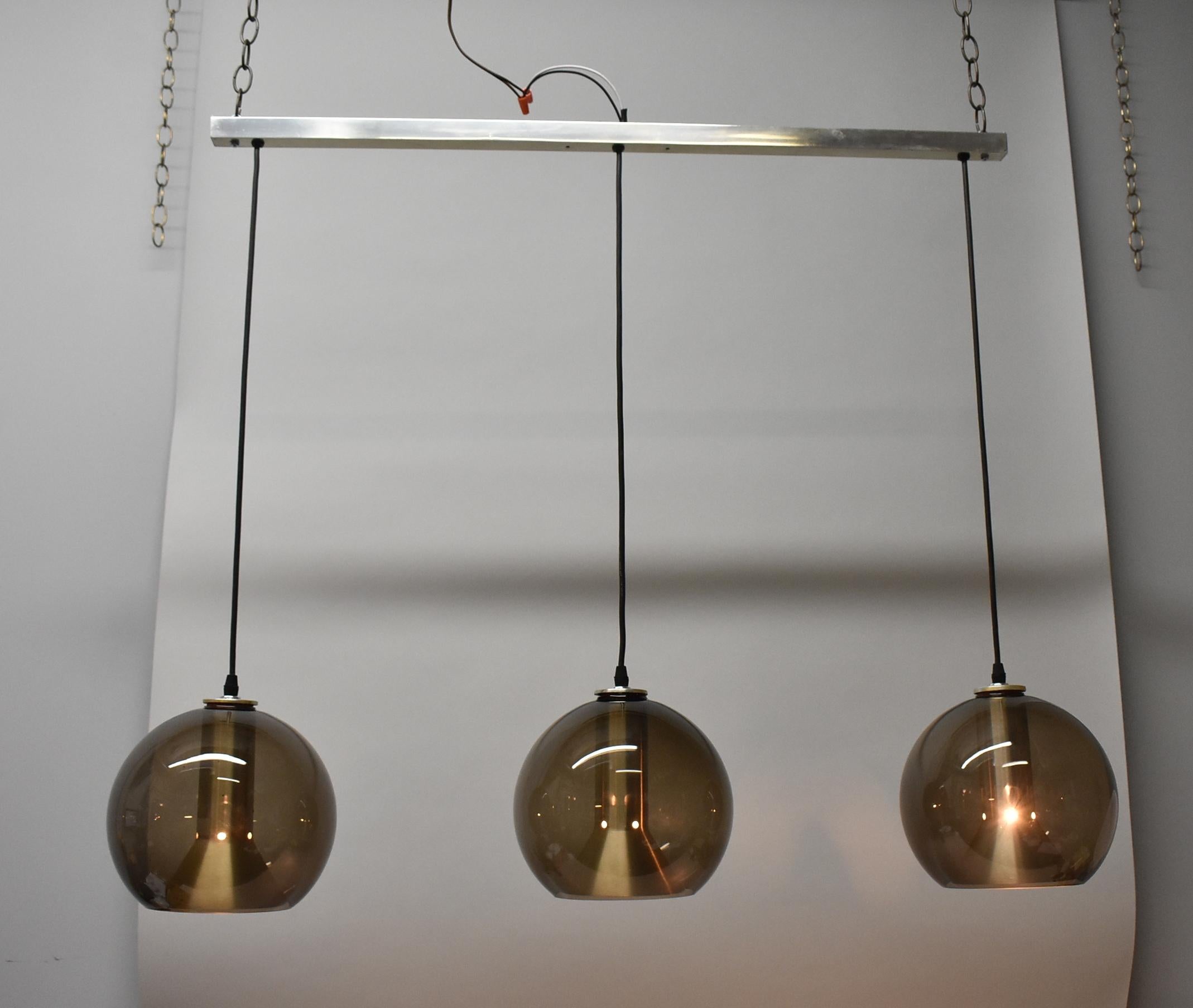 Luminaire de bar moderne du milieu du siècle, conçu par Frank Ligtelijn pour RAAK, Amsterdam. Le luminaire comprend 3 lampes globe de couleur fumée suspendues à une barre de 41