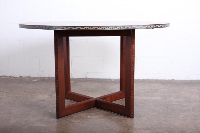 A mahogany dining table with patinated brass trim and Greek key detailed base. Designed by Frank Lloyd Wright for Henredon.

Table measures 48 dia x 29h with three 16
