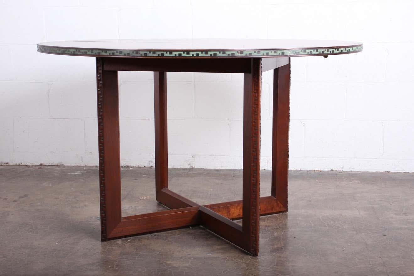 A mahogany dining table with patinated brass trim and Greek key detailed base. Designed by Frank Lloyd Wright for Henredon.

Table measures 48 dia x 29h with three 16