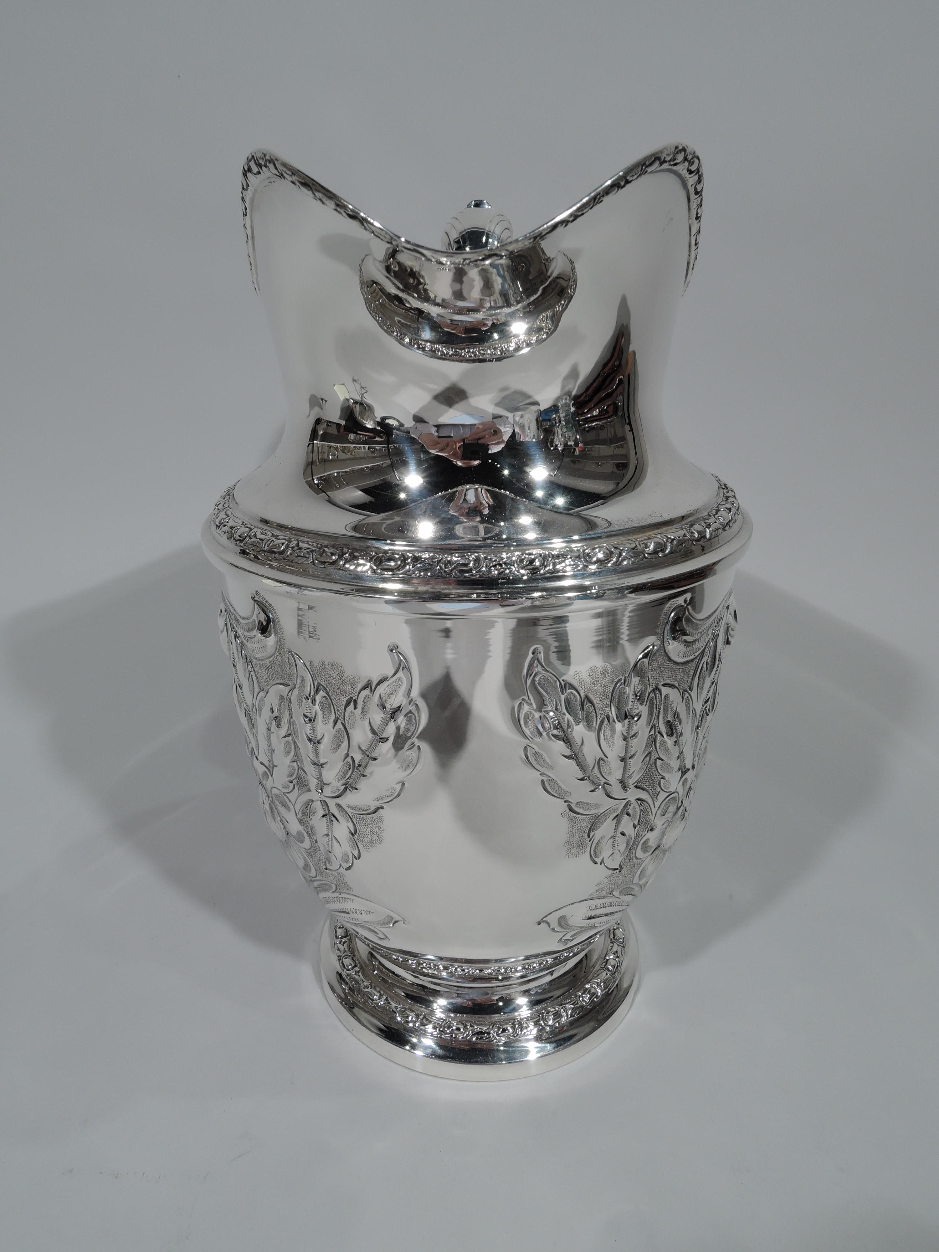 Pretty sterling silver water pitcher in Talisman Rose. Made by Frank M. Whiting in North Attleboro, Mass. Helmet mouth, leaf-capped scroll handle, and stepped foot. Chased floral frames (vacant) and borders. A nice piece in this pattern, which was