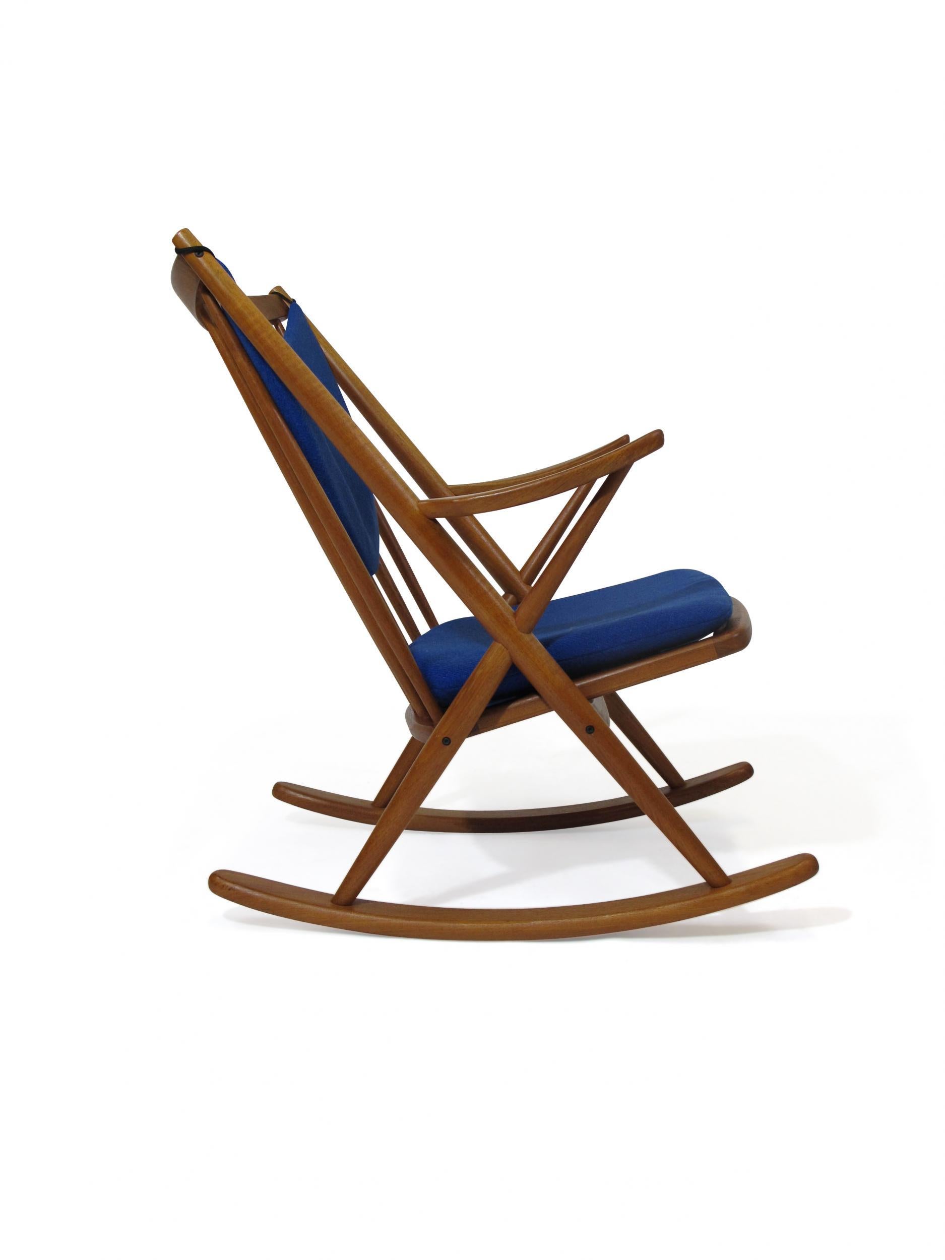 Danish teak rocking chair designed by Frank Reenskaug for Bramin Model 182, circa 1958, Denmark. The rocking chair is crafted of a solid teak frame with spindle backrest, sculpted armrest, and upholstered cushions in the original navy blue wool
