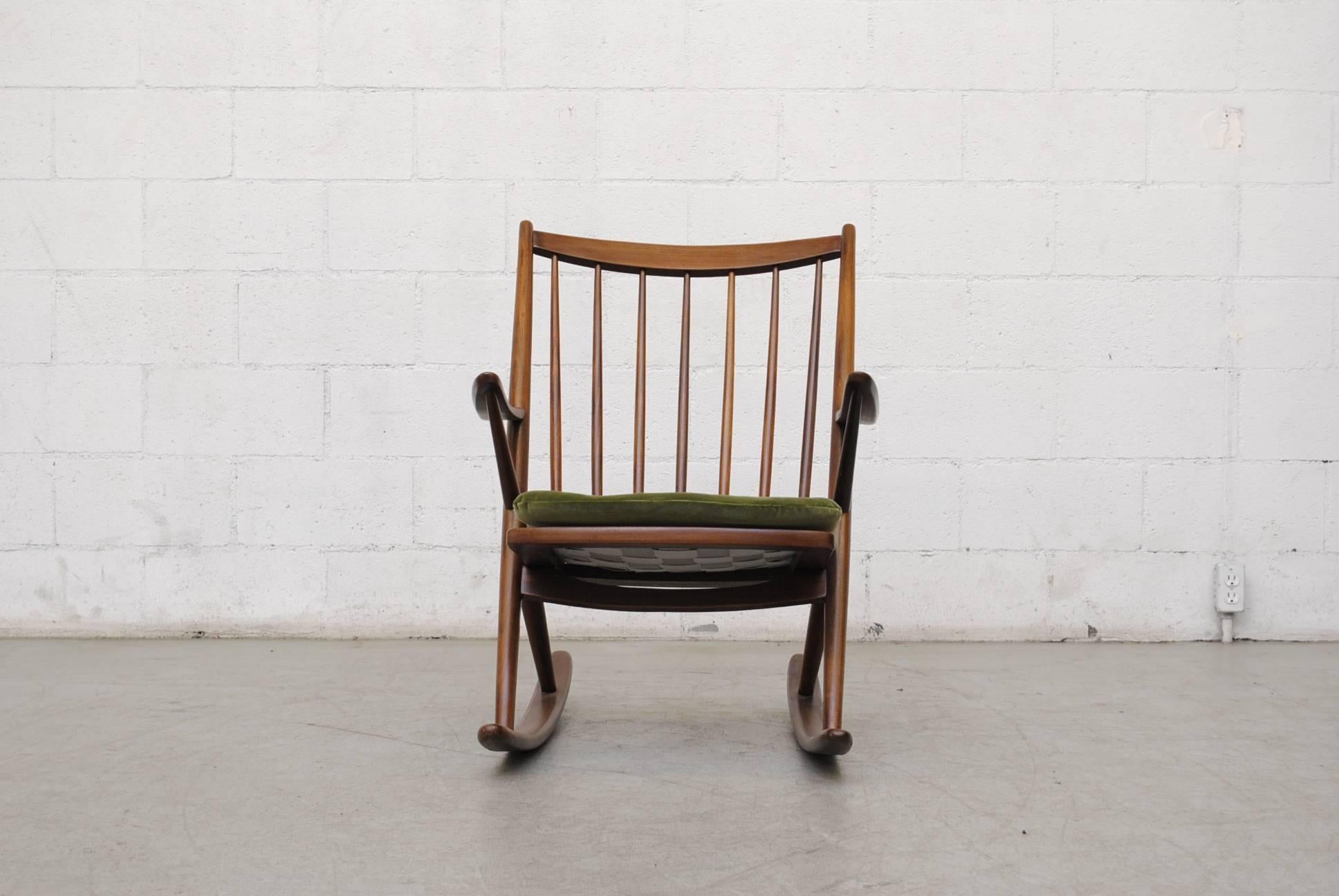 Lightly refinished teak midcentury rocking chair with arms. Spindle back. With new dragon green velvet cushion. In good original condition with wear consistent with its age and usage.