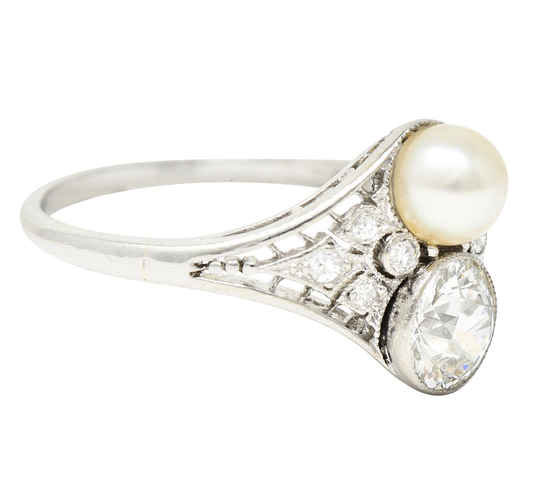 Centering an old European cut diamond weighing approximately 0.72 carat total H color with VS1 clarity. Bezel set North to South with a 5.0 mm round natural pearl - cream with moderate iridescence. Juxtaposed to convey a 'toi-et-moi' motif - French