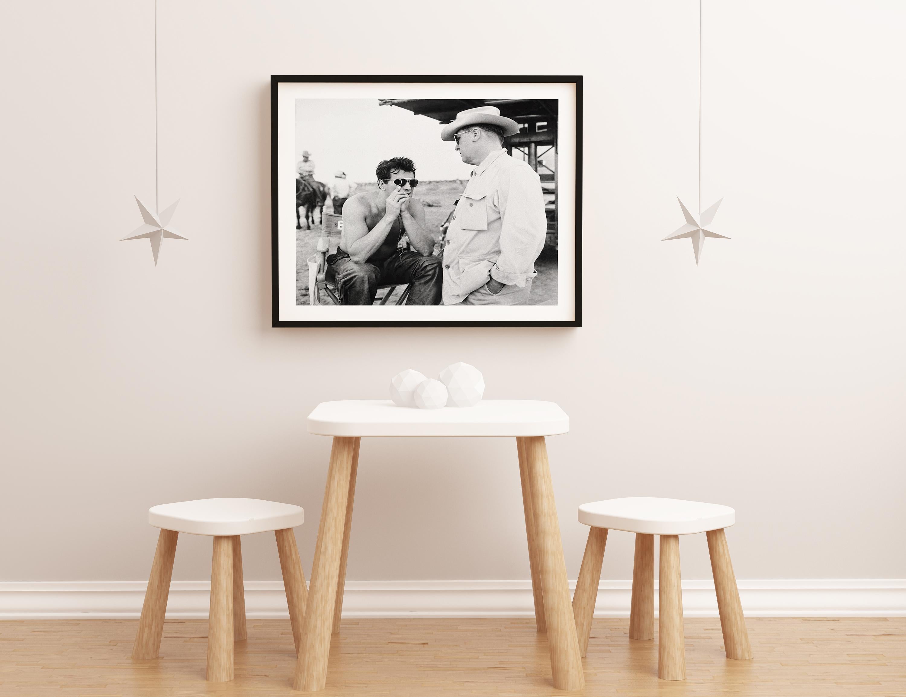 This black and white portrait by Frank Worth features a candid shot of Rock Hudson and George Stevens conversing on the set of 