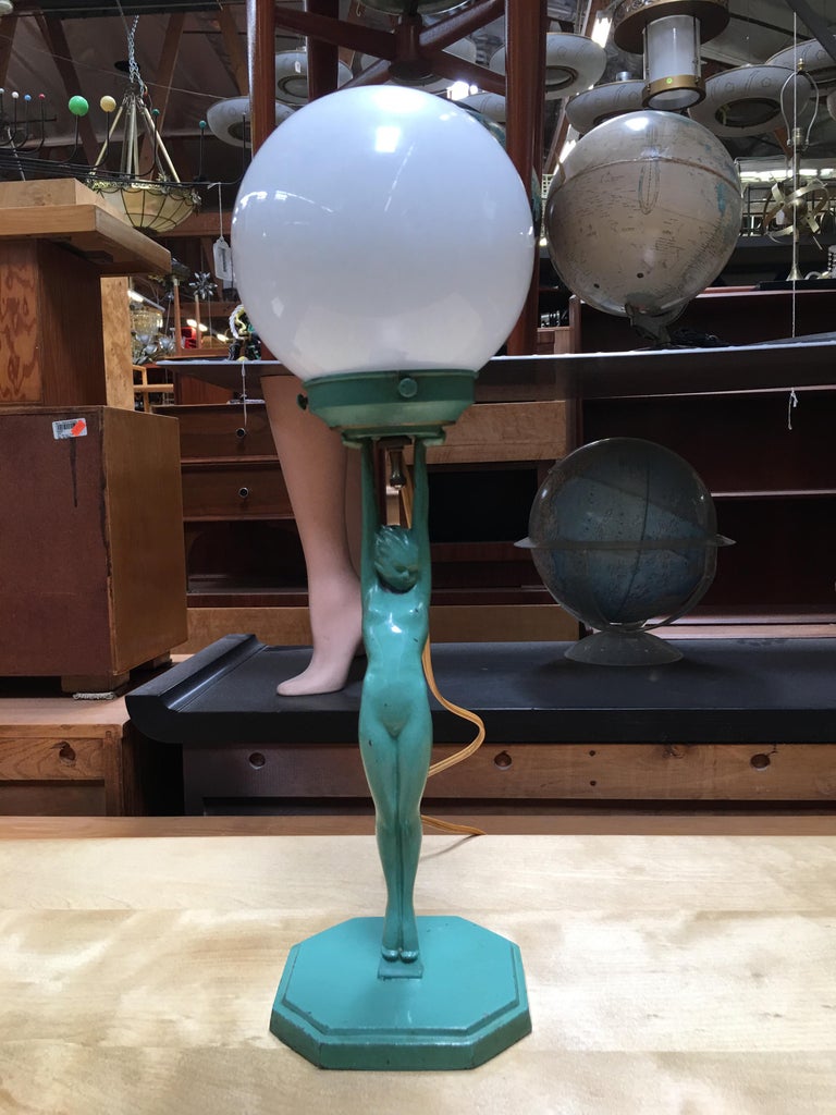 This Frankart model L210 nude spelter metal sculptural table lamp features an Art Deco styled nude female nymph holding up a light. The lamp comes with the original Frankart stepped pointed crackle green glass shade. A crackle glass globe and milk