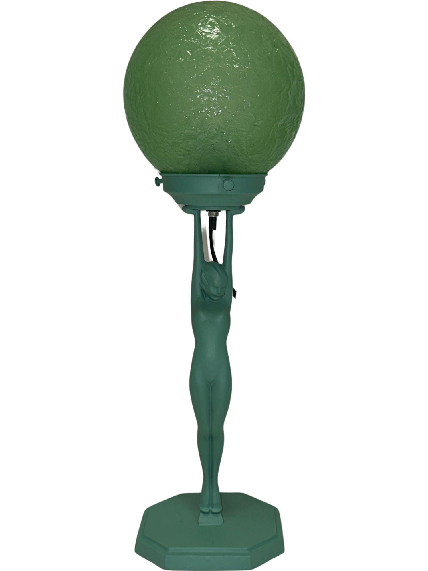 It features an exquisite nymph cradling a green glass lampshade adorned with a 'cracked ice' texture, all elegantly perched atop an octagonal stepped base. This base includes attached cardboard and felt for stability, with a charming verdigris