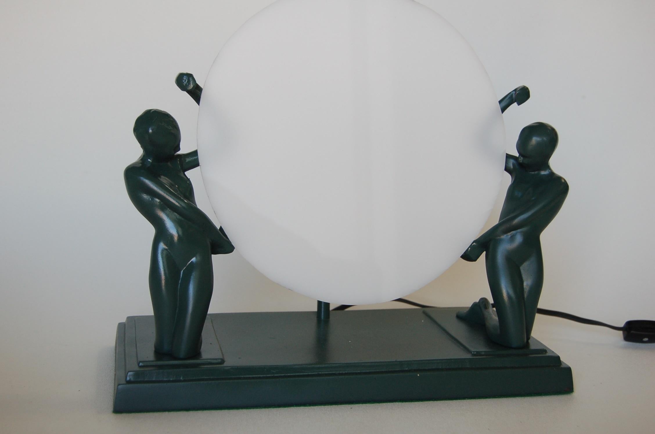 Striking Frankart style accent table lamp featuring kneeling nude female figurines holding plexiglass disc in green. Toggle light switch.

Measures 12.5 wide x 6