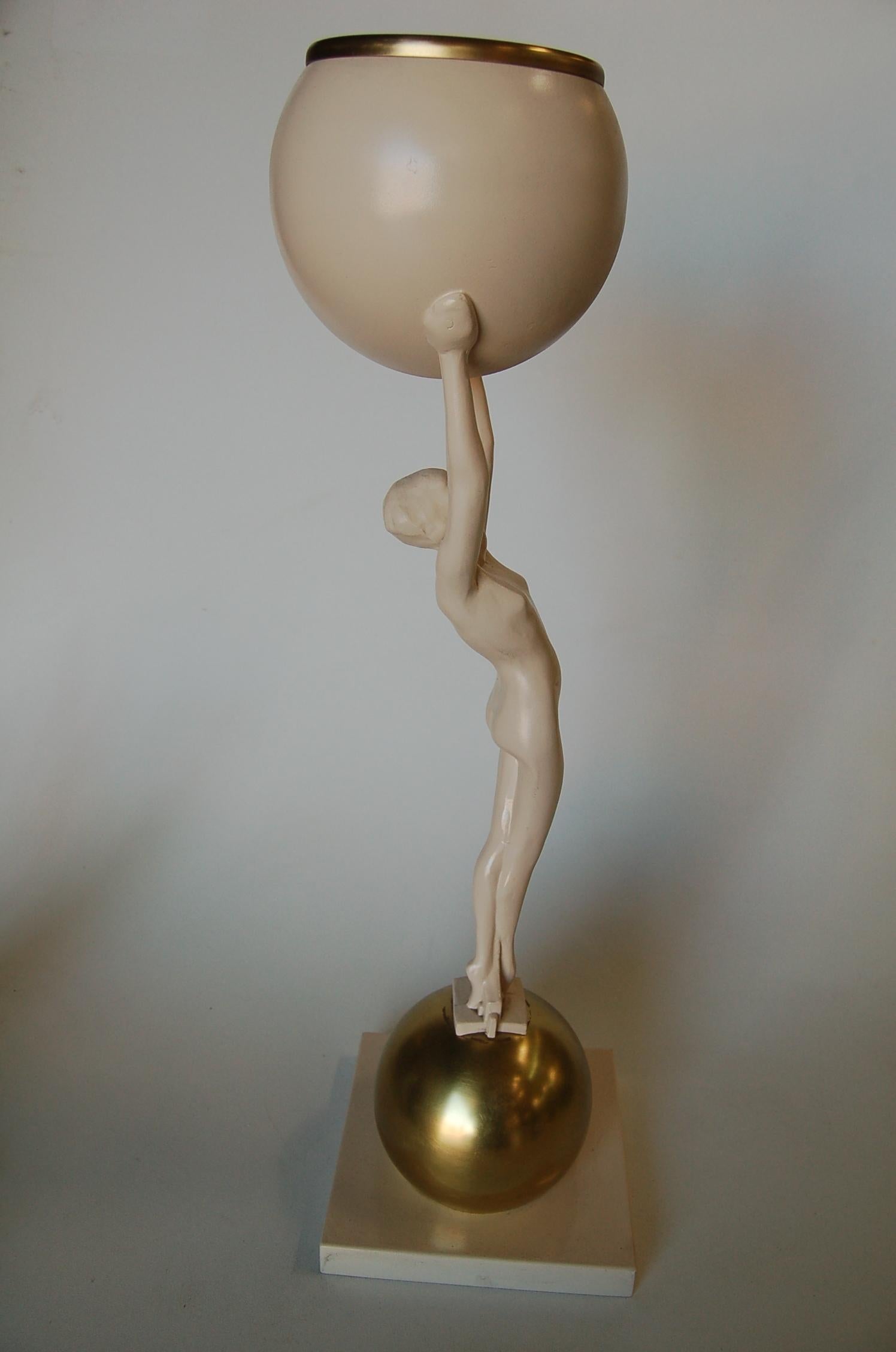 Striking Frankart-style table lamp featuring a nude female figure on top of a gold ball holding a white ball that contains a light. 

Measures 8