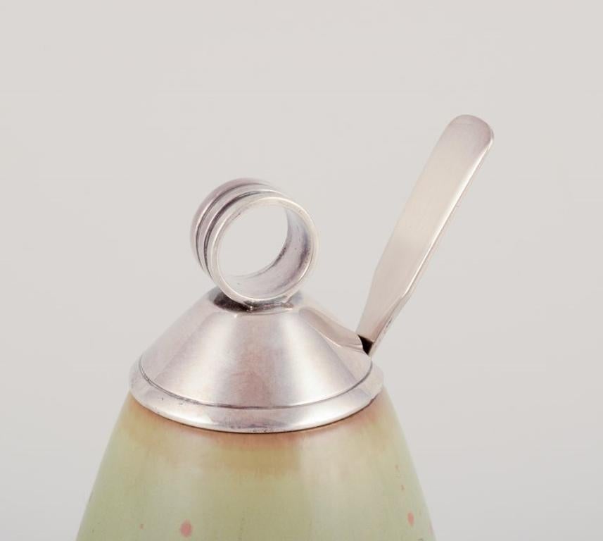 Frantz Hingelberg and Royal Copenhagen.
Art Deco ceramic jam jar with matching lid and spoon in sterling silver.
Glazed in greenish shades with brown accents.
Model: 20393
1930s.
Marked.
In perfect condition.
First factory quality.
Dimensions: