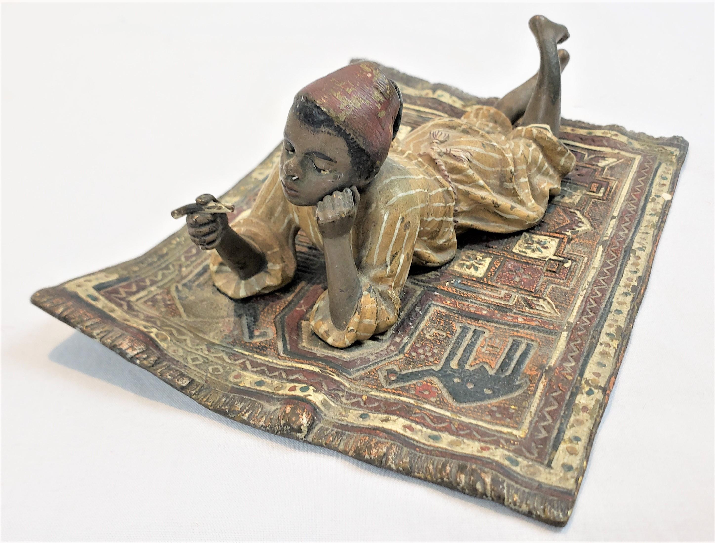 This sculpture was done by the renowned Franz Bergman of Austria in approximately 1900 in his signature Bessarabian style. The study is composed of cast bronze with a cold-painted finish depicting a young Arab boy laying on a carpet smoking a cigar.