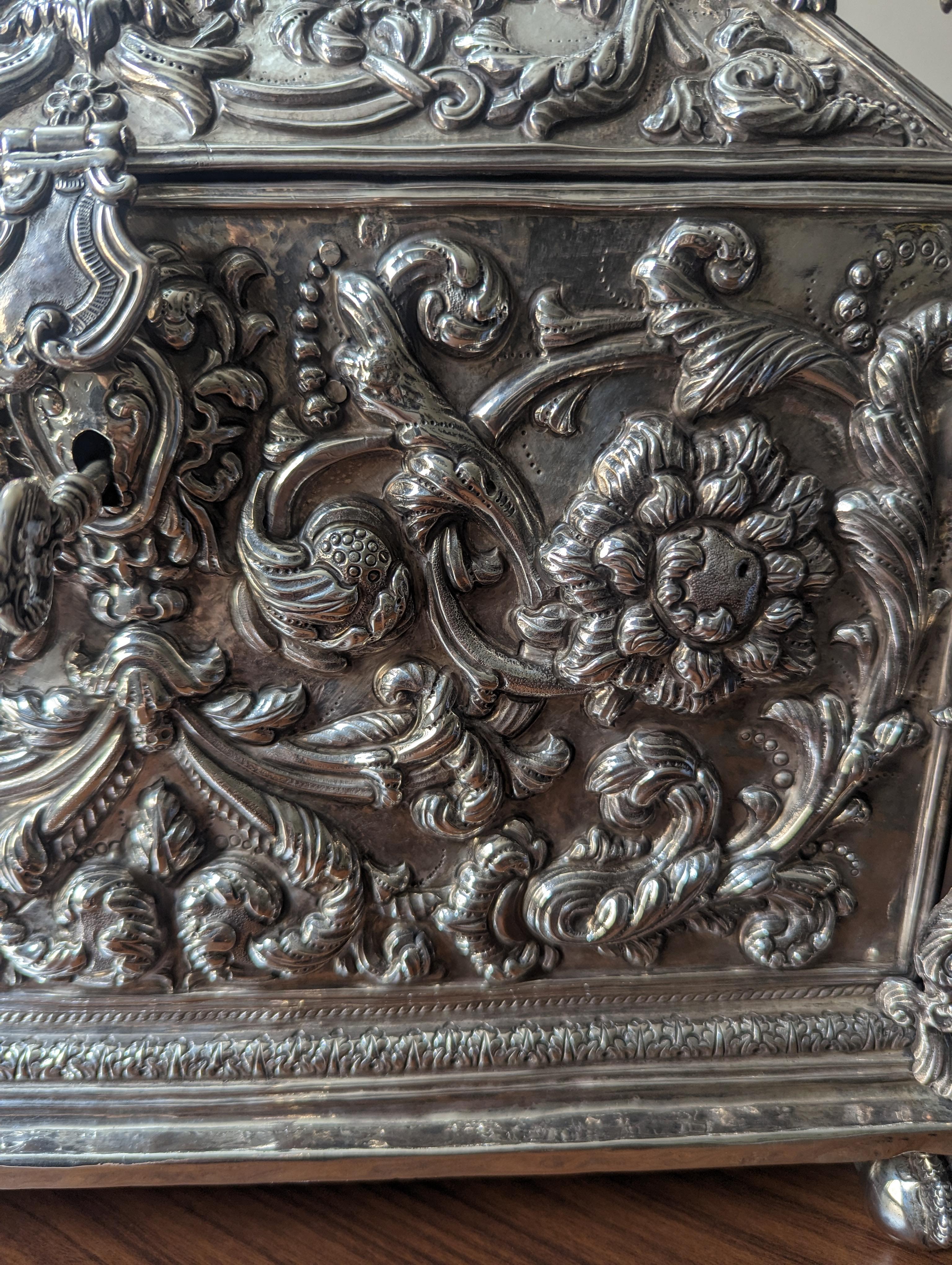 Este impresionante cofre ornamentado de plata de ley es una auténtica obra maestra, hecha a mano con exquisita atención al detalle por los mejores artesanos bolivianos. Los laterales y la tapa están ricamente decorados con elaborados motivos