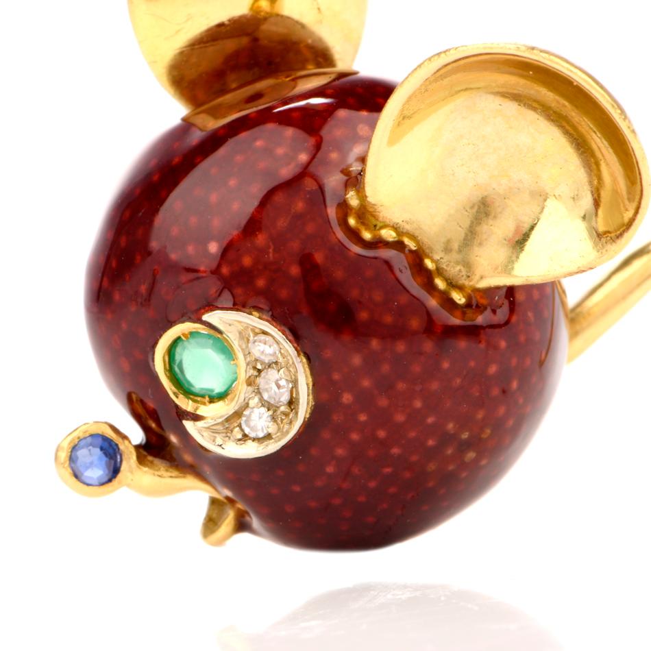 This whimsical mouse pin brooch is crafted in solid 18-karat yellow gold, weighing 15 grams and measuring 40mm long x 39mm wide. Showing  a mouse head and tail, the face is in Italian red enemal. The eyes and nose are prong-set with one round blue