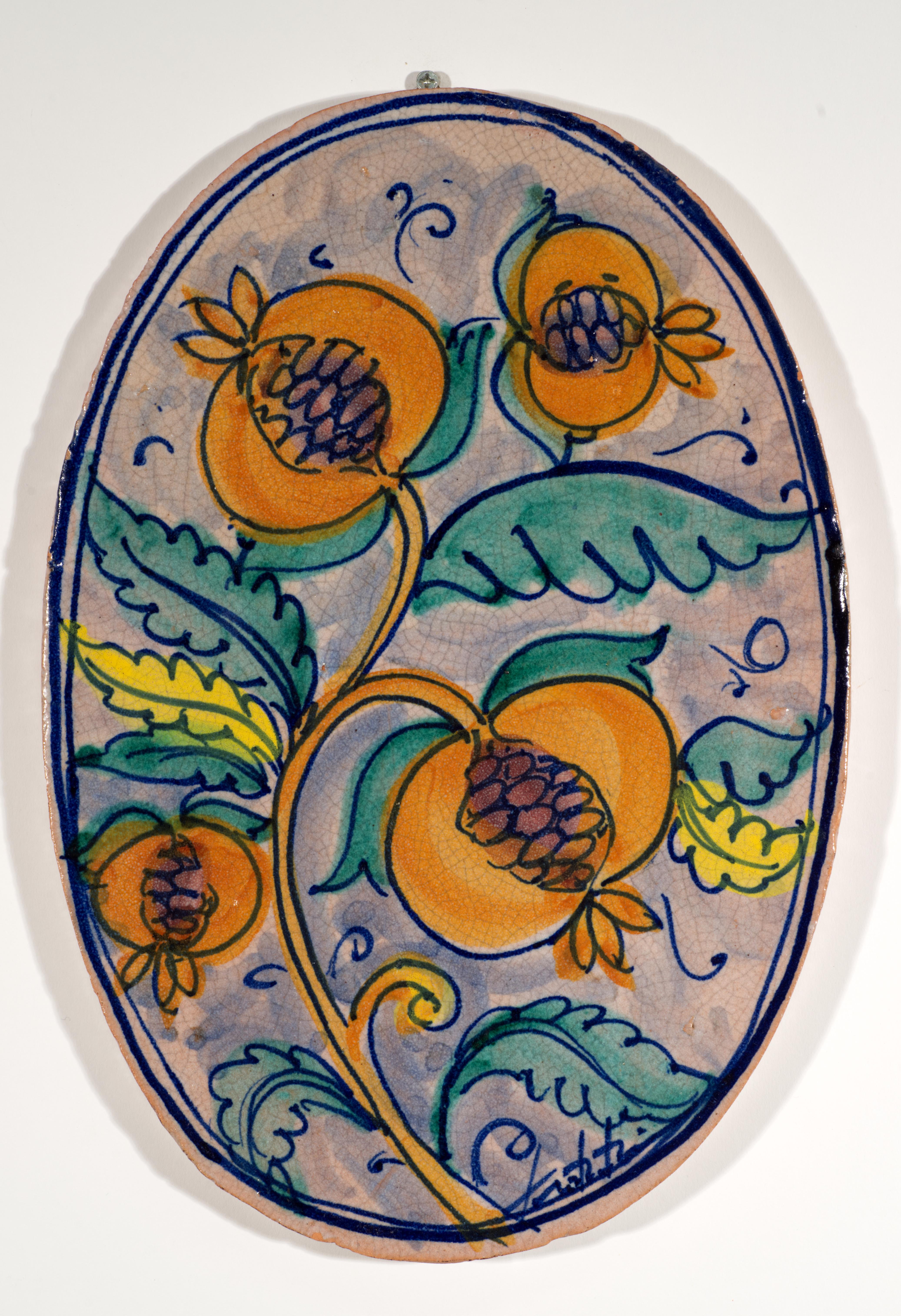  Plaque murale ou carreau ovale vintage en céramique présentant un décor abstrait moderniste avec des branches de fruits orange et des feuilles vertes et jaunes sur fond bleu-vert. La forme ovale de la plaque fait écho aux lignes douces, aux fruits