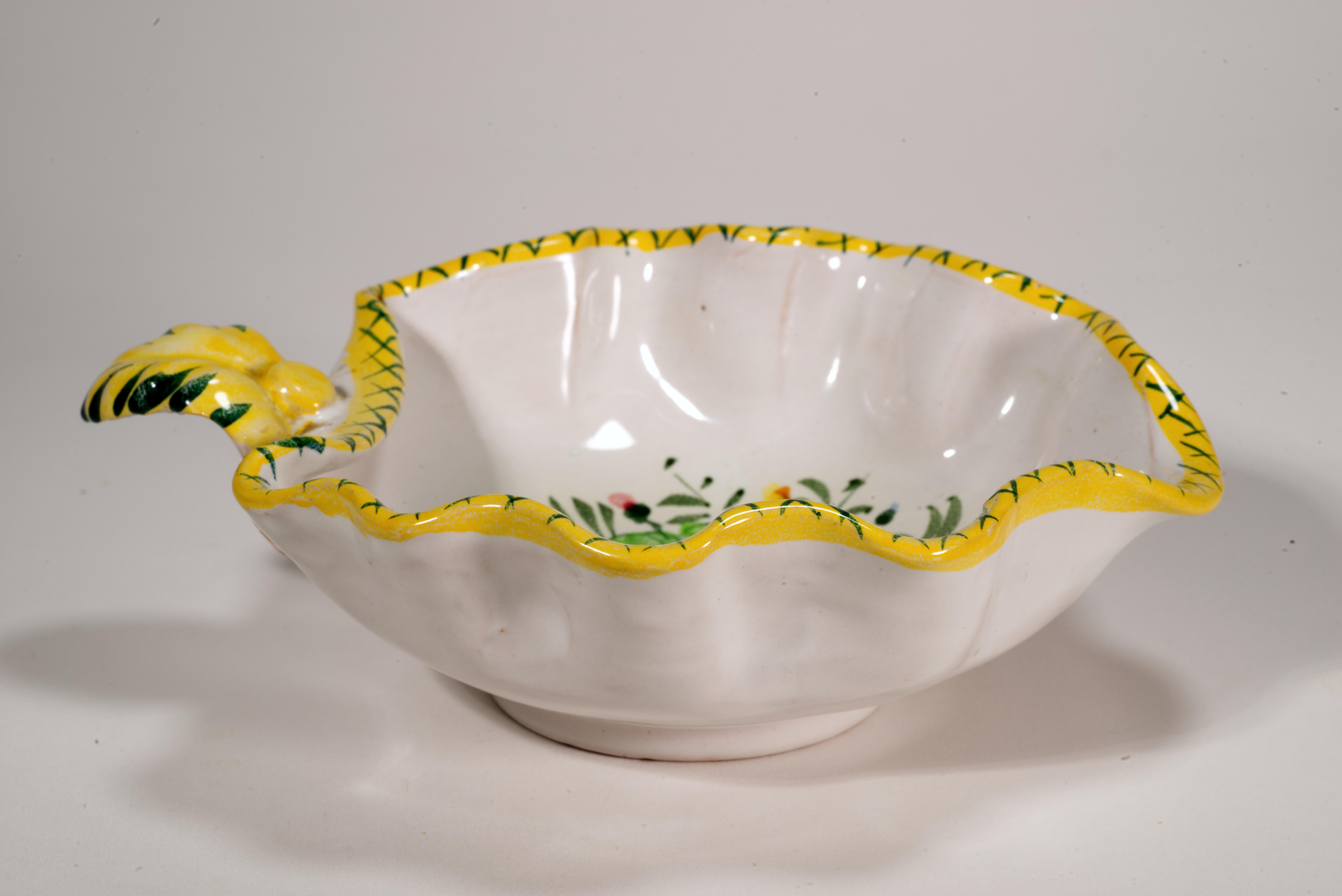  La rara ciotola vintage è decorata con fiori e foglie stilizzati dipinti a mano. La ciotola presenta un bordo asimmetrico modellato a mano e un piccolo manico figurativo a forma di foglia. Il bordo è accentuato da una fascia gialla con motivi