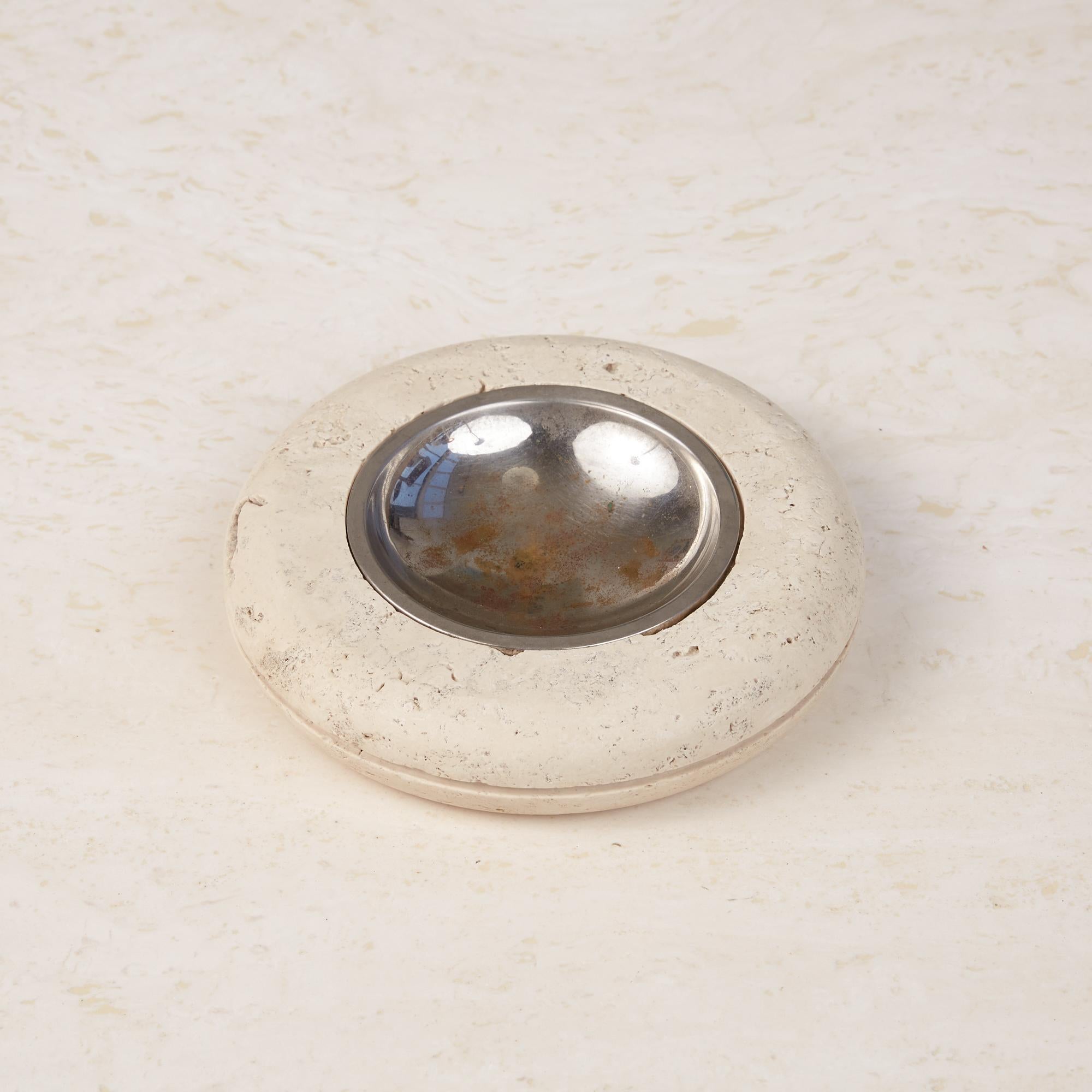 A tire shaped round travertine ashtray by Fratelli Mannelli, Italy, circa 1970s, has a honed to a matte finish and with a scooped metal dish that sits in a recess in its center. It has a groove carved around its circumference at the apex of its