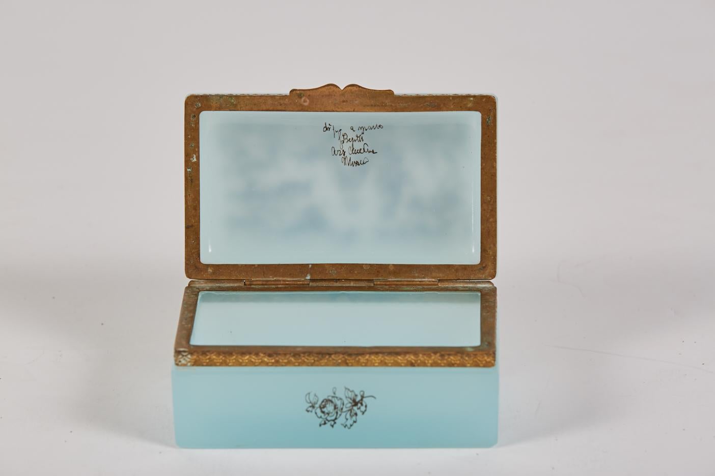 Fratelli Murano pale blue opaline glass hinged box with enameled decoration and gilt metal mount. The exterior enameled decoration shows a man and woman in 18th century attire in a woodland setting. 
 The interior of the box bears the signature of