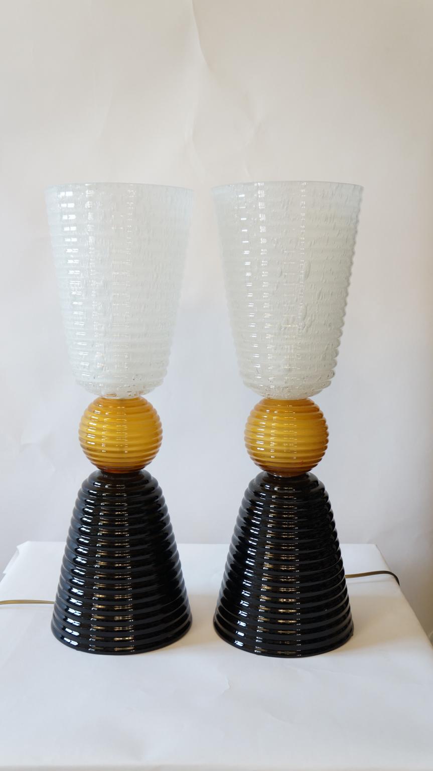 The lamp you can see in the picture is very simple but impressive. It is precisely the striking complementarity
between black and white, divided by amber, that makes it so elegant. It develops with two symmetrical cups divided by a ribbed sphere.