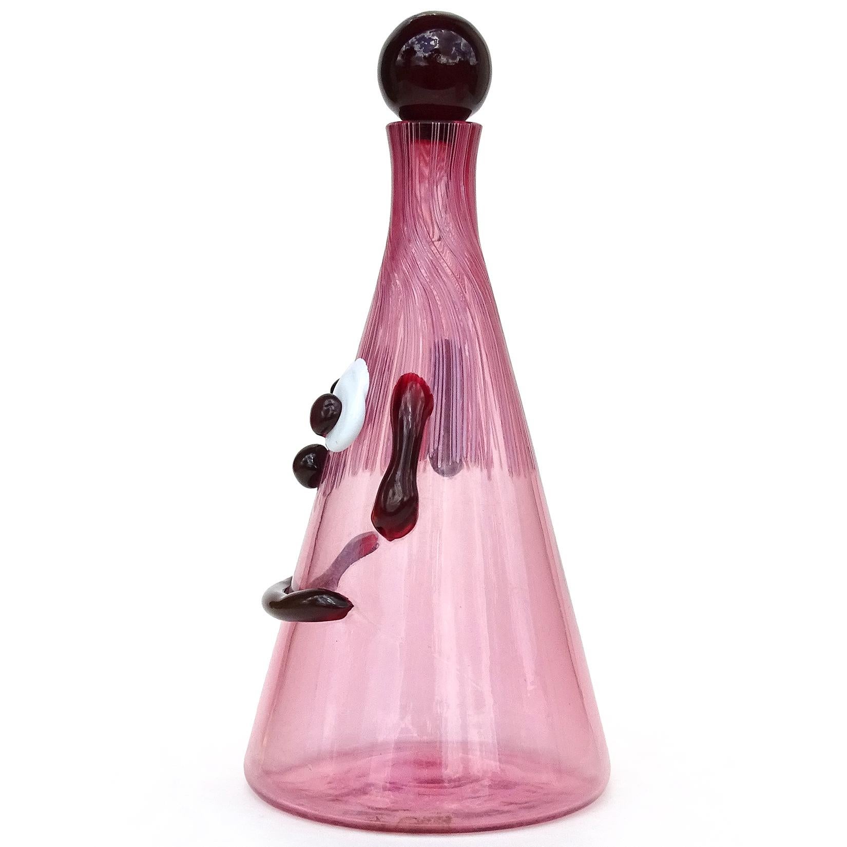 Cute and rare, vintage Murano hand blown Italian art glass cranberry pink clown face decanter, with red accents. Documented to the Fratelli Toso Company. The bottle has droopy ears, wide eyes, a big smile, and threads of light pink glass for the