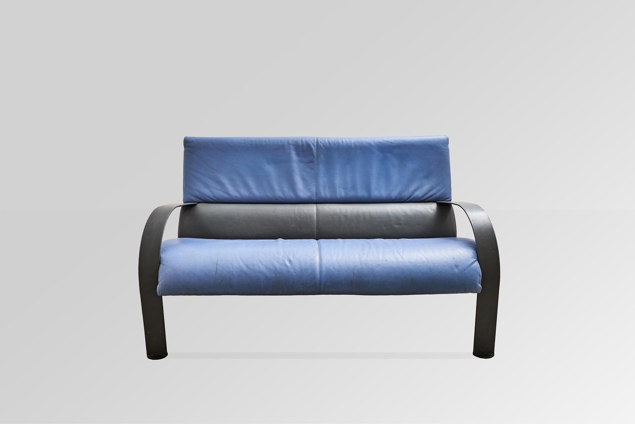 Ce canapé deux places saisissant de FRAU présente une combinaison audacieuse de cuir polychrome bleu et noir, élégamment contrastée par un cadre métallique épuré. Le design incarne à la fois la sophistication et le confort, avec une fabrication de