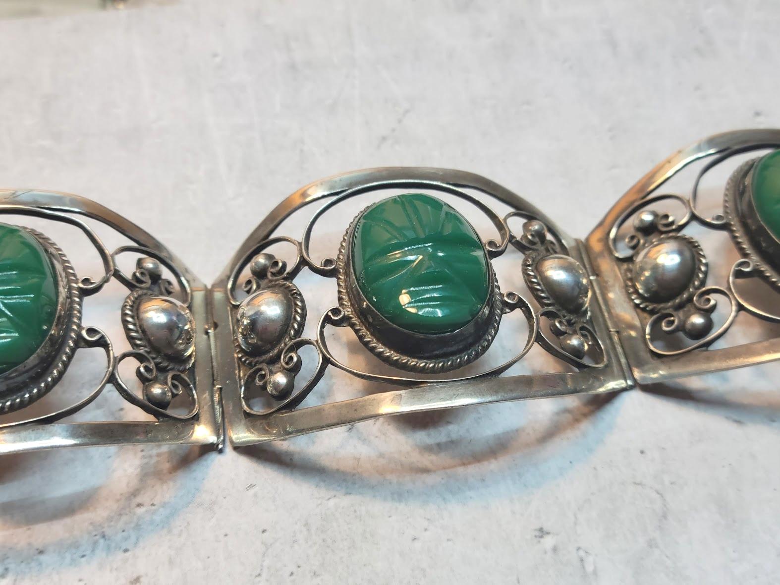 A Mexican bracelet comprised of fine sterling silver with green onyx cabochons in the form of Aztec masks.
The bracelet has decorative silver panels with heavy beading, swirls, and oval onyx Aztec masks. This vintage panel bracelet was made in