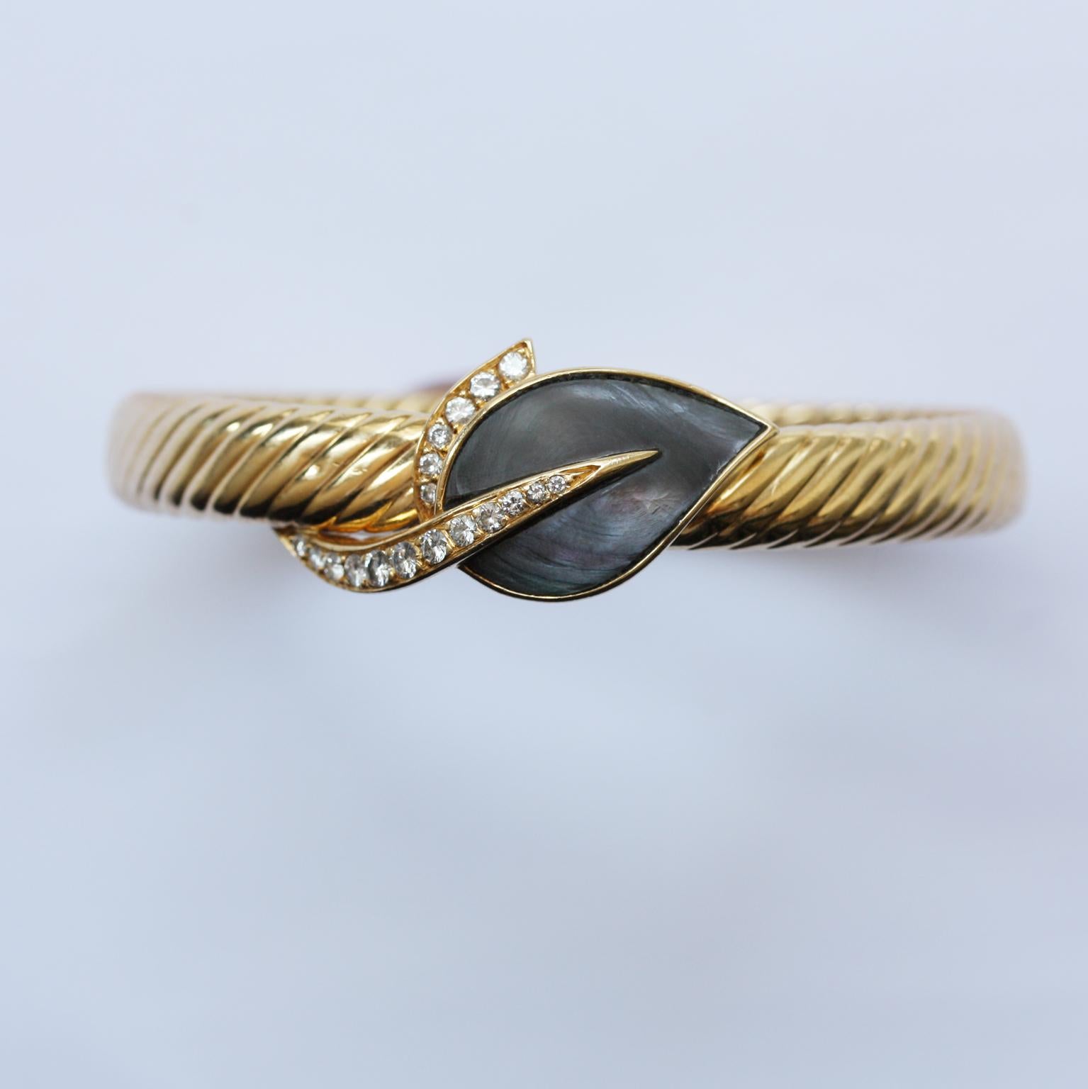 An 18 carat gold ribbed bangle with a grey mother of pearl or abalone and diamond leaf in the hidden lock, signed: Fred, Paris, circa 1980, France (small dent).

weight: 27.46 gram.
size: 16 - 16.5 cm.
width: 8 - 16 mm