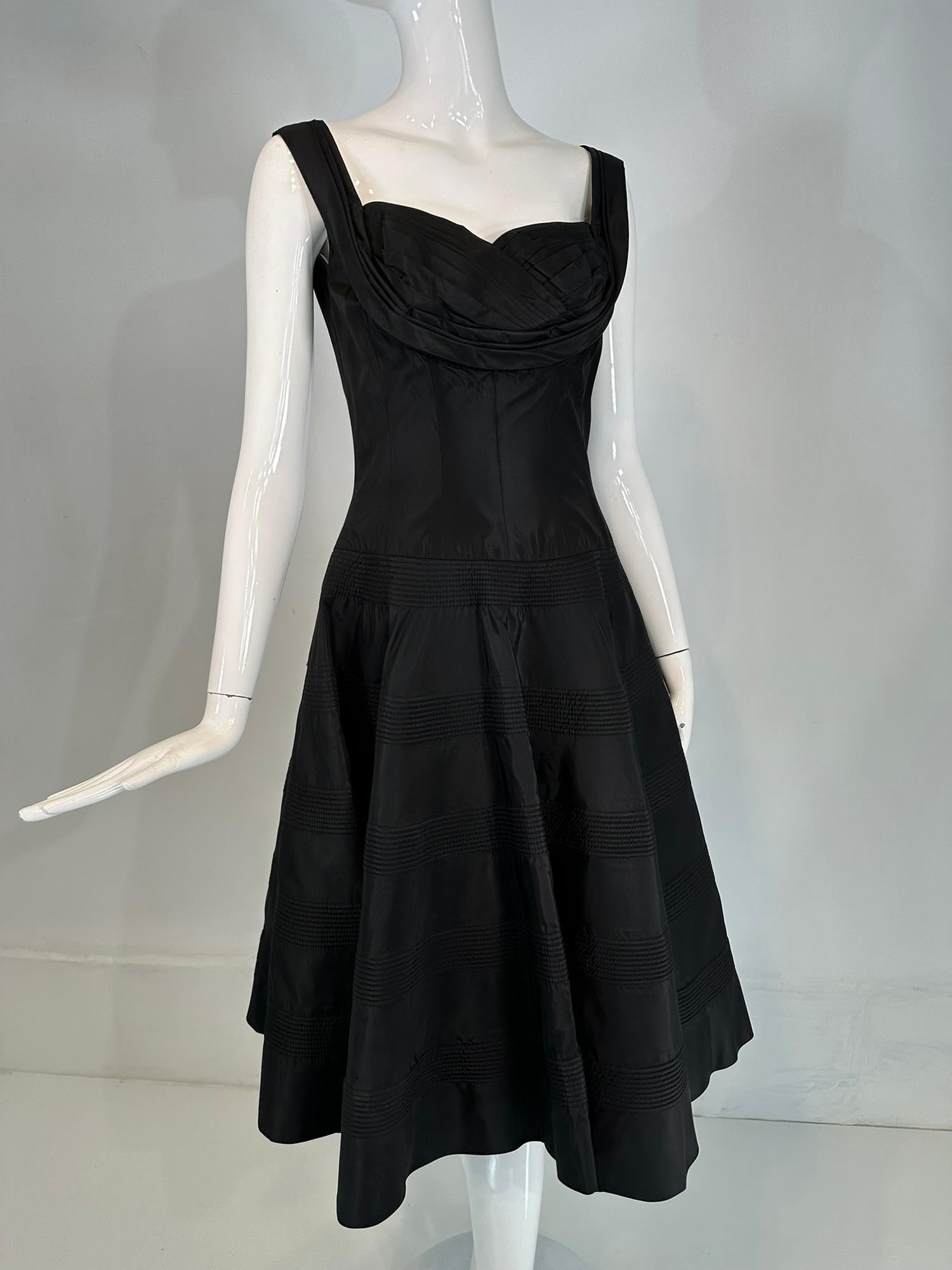 Fred Dance Originals 1950s robe de cocktail en taffetas noir avec corsage à découpes et jupe circulaire matelassée. Robe sans manches à encolure dégagée et à bretelles plissées qui épousent les épaules. Le corsage est ajusté, avec un décolleté en