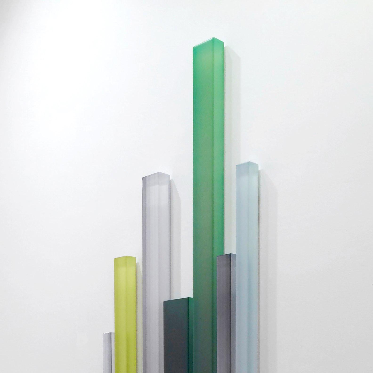 Thicket is a large-scale mixed media work constructed of luminously painted bars of cast acrylic. The white negative space on the wall allows the green, blue and gray color forms to float, and create the illusion of movement. The colors shift