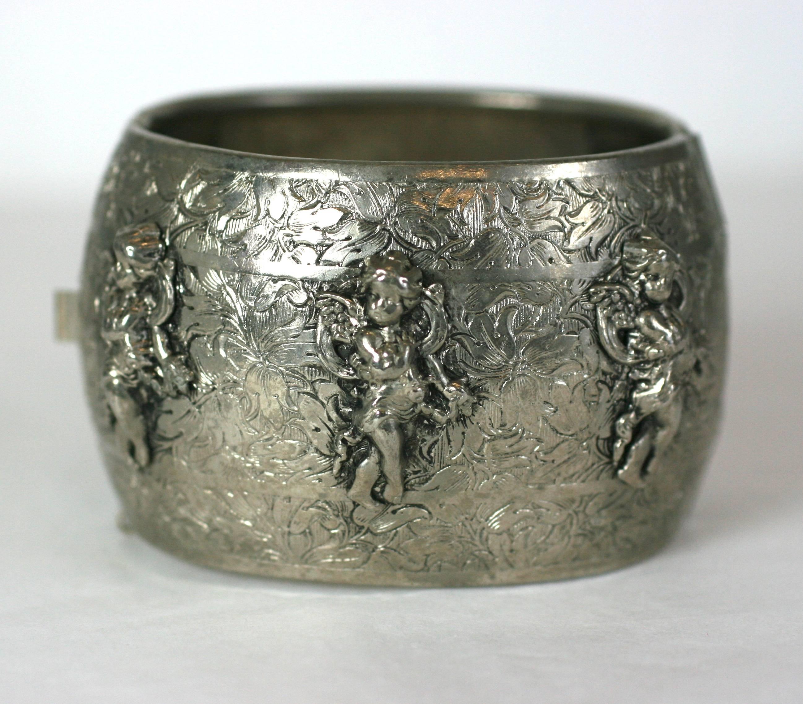 Frederich Putti decorated bombe hinged cuff bracelet of antiqued silvered metal etched with a scrolling floral motif. The finely detailed cherubs draped in ribbon garlands and bows. Hinged closure with safety chain. 1950 USA. 
Excellent  Condition.