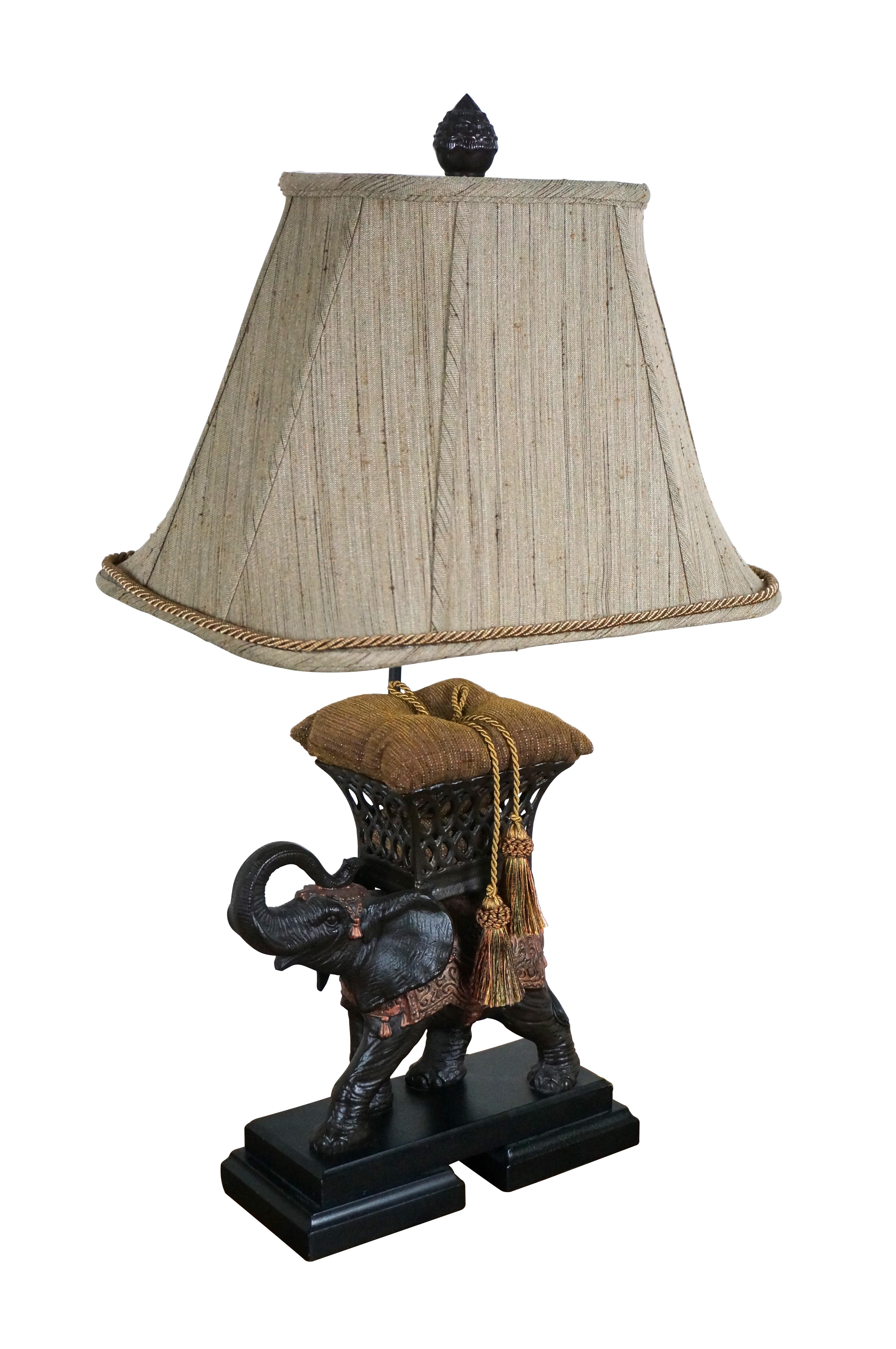 Vintage late 20th century Frederick Cooper bronze table lamp in the shape of an Indian elephant draped with gilt saddle blankets with a lucky raised trunk and a pillow-filled howdah on its back. Black rectangular stepped base. Includes harp, finial,