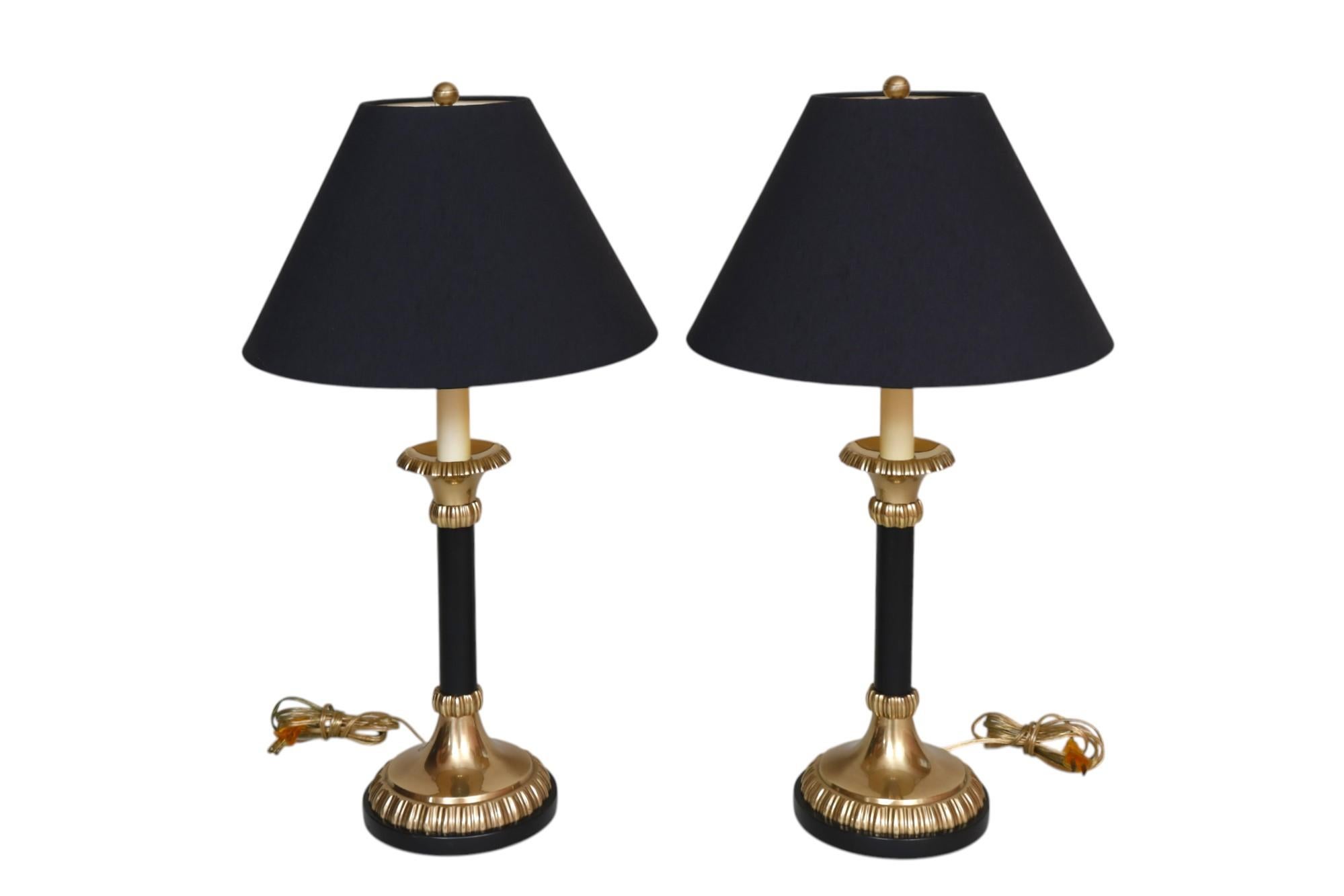 Une paire de lampes chandelier en laiton par Frederick Cooper de Chicago. Les abat-jours originaux en lin noir sont fixés par des boules en laiton. Les colonnes noires mates sont surmontées d'un égouttoir en laiton pressé en forme de frange et se