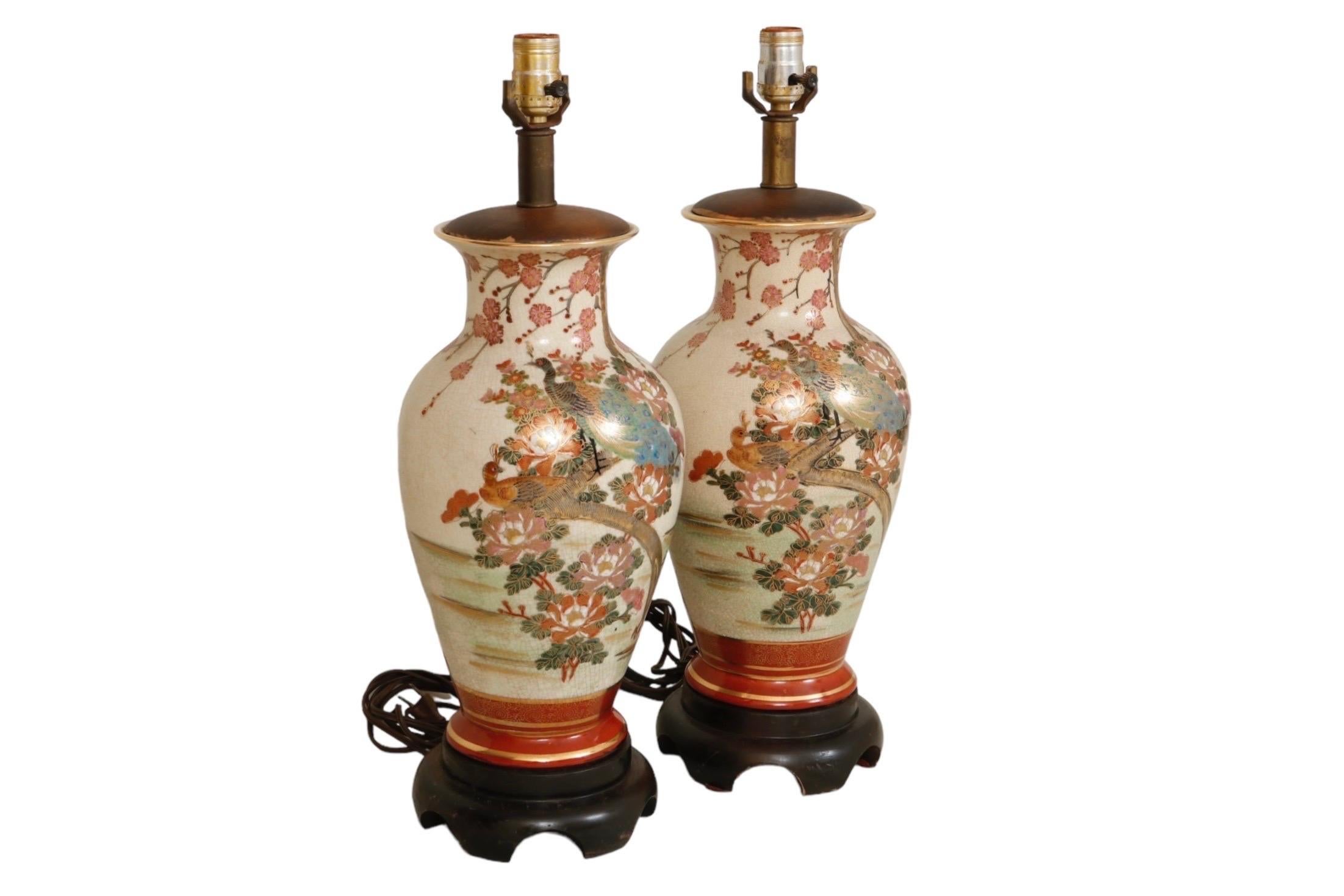 A pair of hand painted chinoiserie table lamps made by Frederick Cooper. Porcelain vases are decorated with a peacock and peahen, nestled among roses beneath a cherry blossom tree. Details are outlined in gold, and finished with a craquelure glaze.