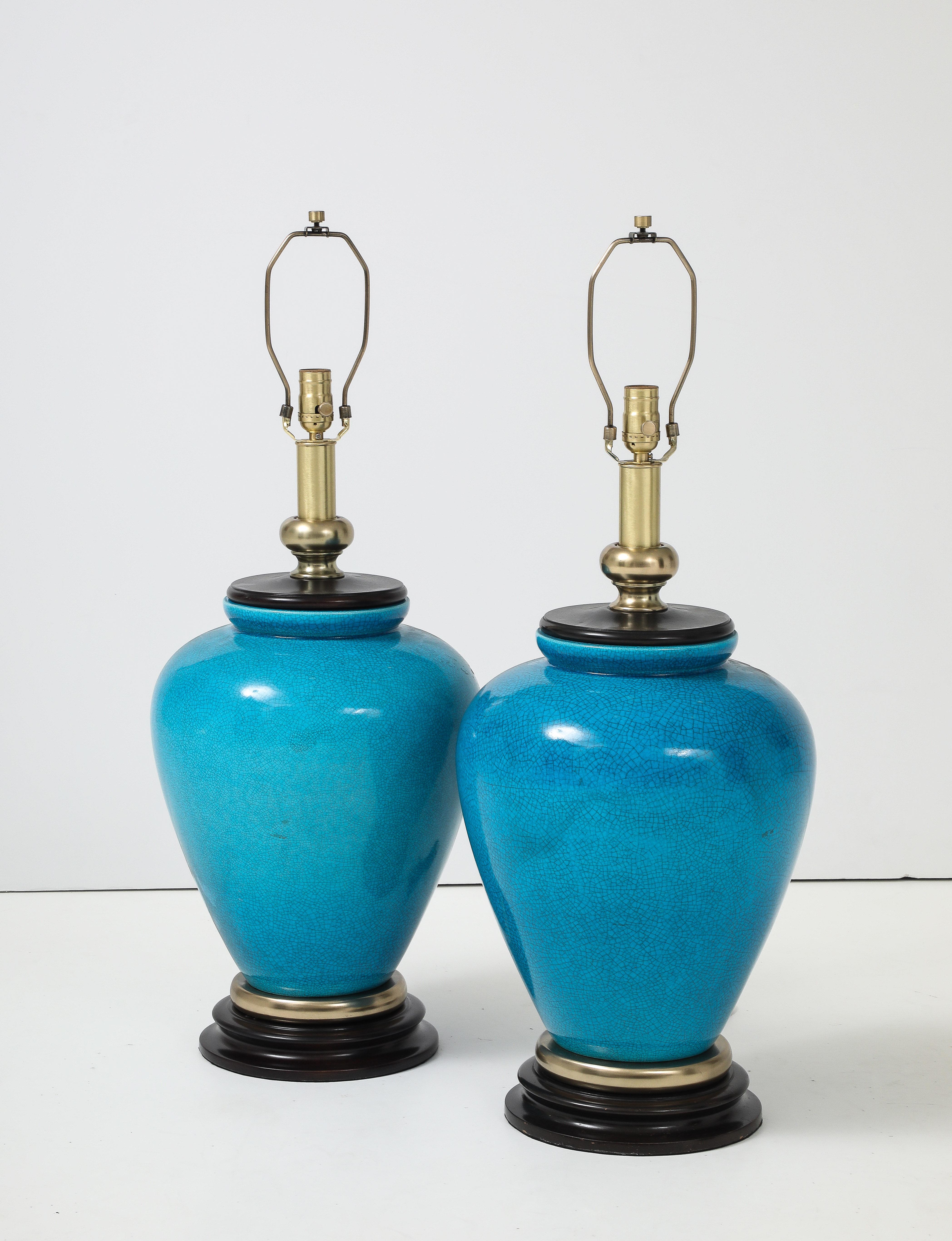 Pair of Turquoise glazed porcelain urn shaped lamps wih satin brass accents, sitting on turned ebonized wood bases. Lamps have been rewired for use in the USA using dark brown fabric cords. 100W bulbs, higher wattage may be used if using LED bulbs.