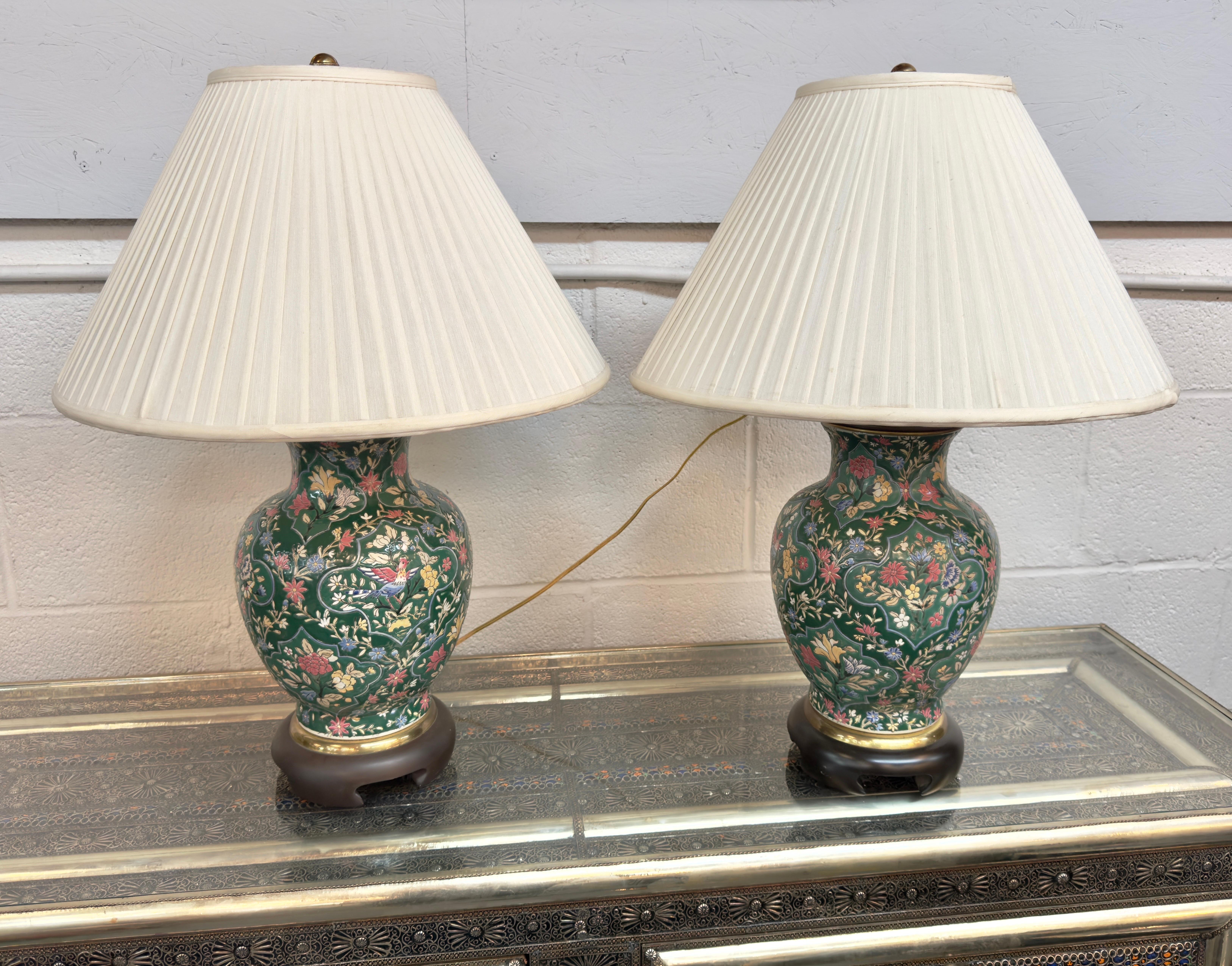 A pair of Frederick Cooper Chinoiserie style table lamps. Adorned with a captivating floral motif, each lamp boasts a bird motif in the center and is delicately hand-painted onto fine porcelain. The lush green hues, complemented by accents of serene