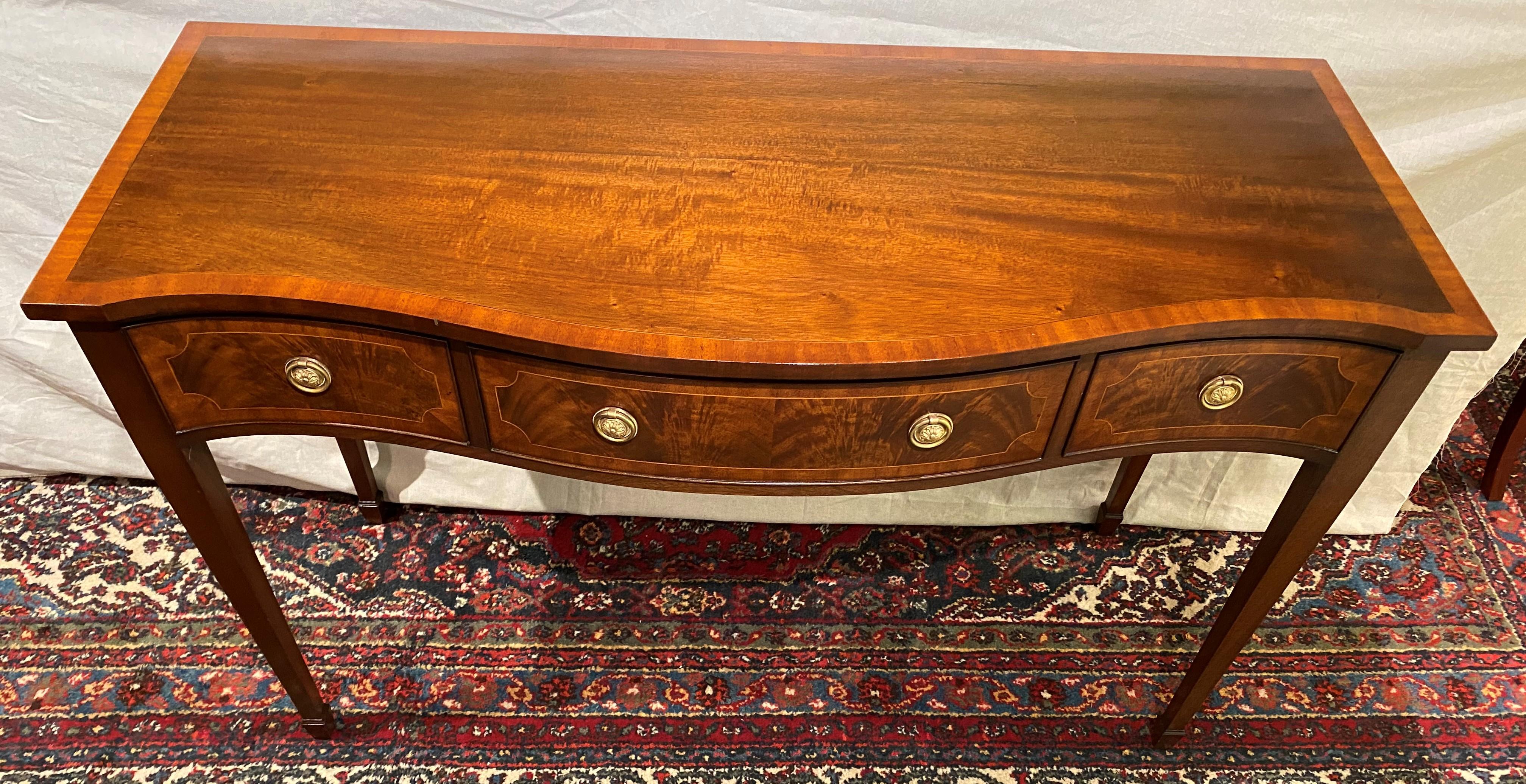 A fine English mahogany console table by Frederick Tibbenham of Ipswich, England, with crossbanded conforming top surmounting three fitted dovetailed cockbeaded frieze drawers with crotched mahogany veneer, satinwood banding and punched floral ring