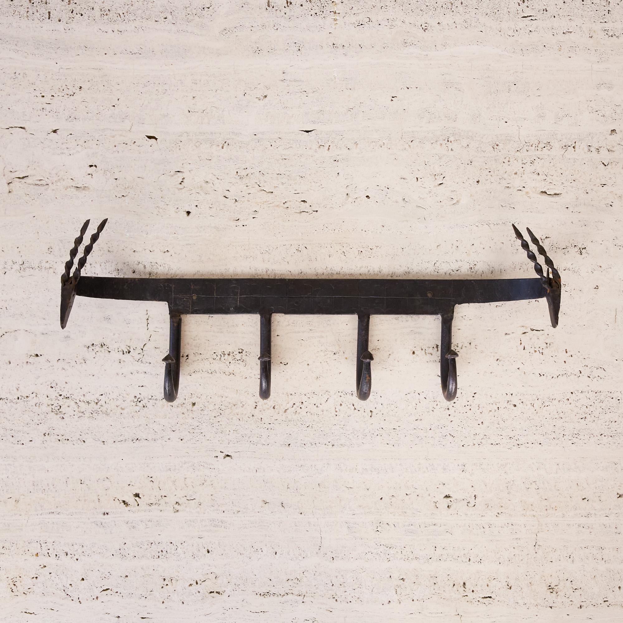 Frederick Weinberg style coat rack. The coat rack features a curved iron strip with four looping iron hooks that extend from below the etched center panel. Both curved ends of the piece feature primitive ibex heads with twisted strips of metal that