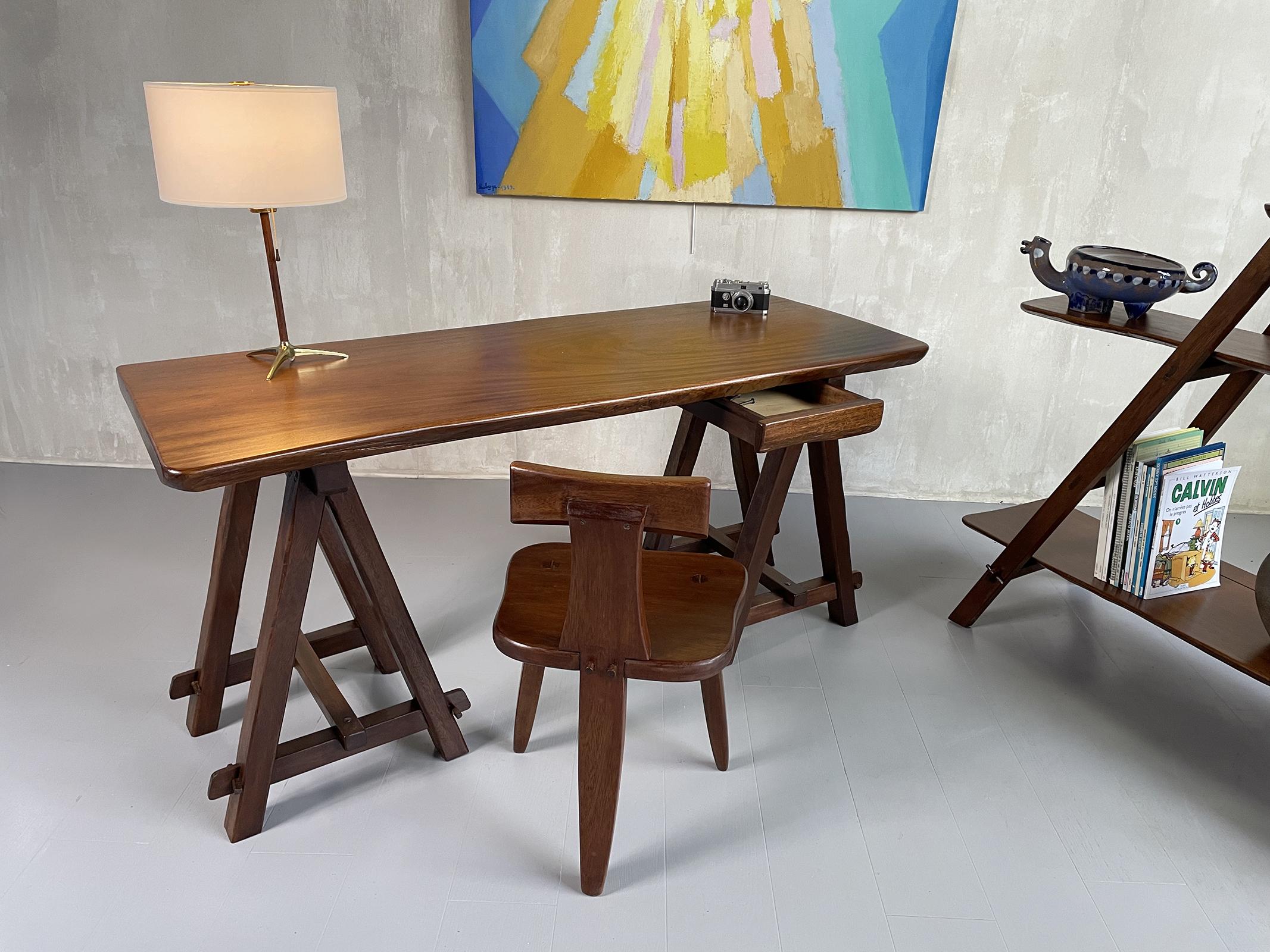 Desk, bookcase and tripod chair in solid mahogany, Circa 1960.
The trestle desk has a 5 cm thick top, a drawer is placed on the right. The bookcase is made up of ladder uprights on which three asymmetrical shelves rest.
The furniture designer has