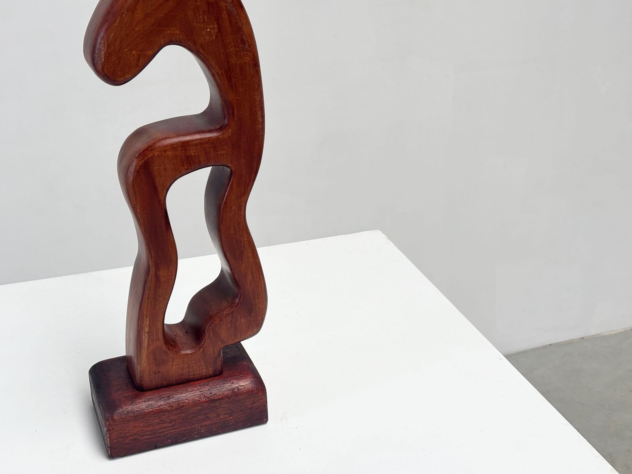This signed abstract freeform wooden sculpture was most likely created in the 1980s by an unknown artist. Despite the mystery surrounding its maker, the craftsmanship and quality are evident. Its playful shape and warm tones make it a charming