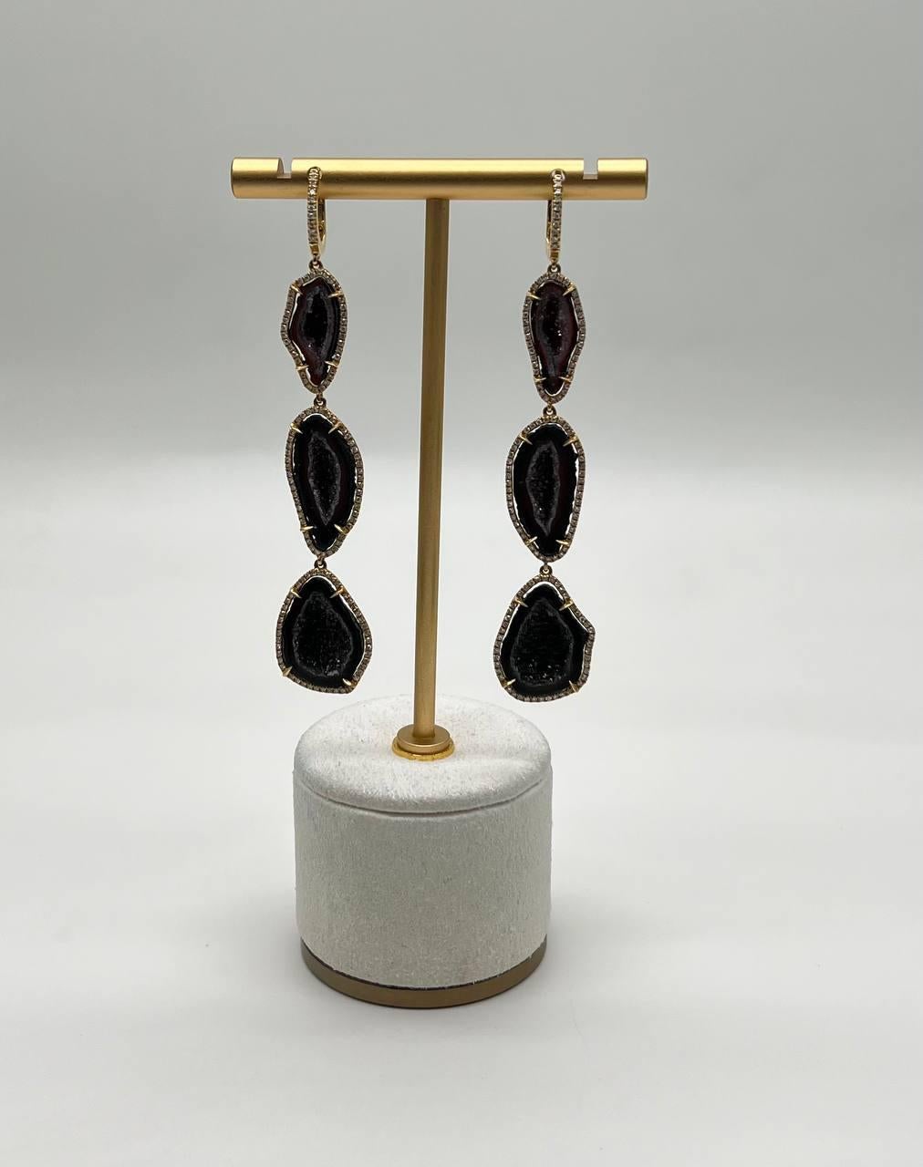 Discover the allure of our exquisite earrings, crafted with precision and elegance.

These captivating earrings feature a trio of dark, organic-shaped brown black druzy quartz, each encased in a delicate halo of shimmering diamonds. The stones are
