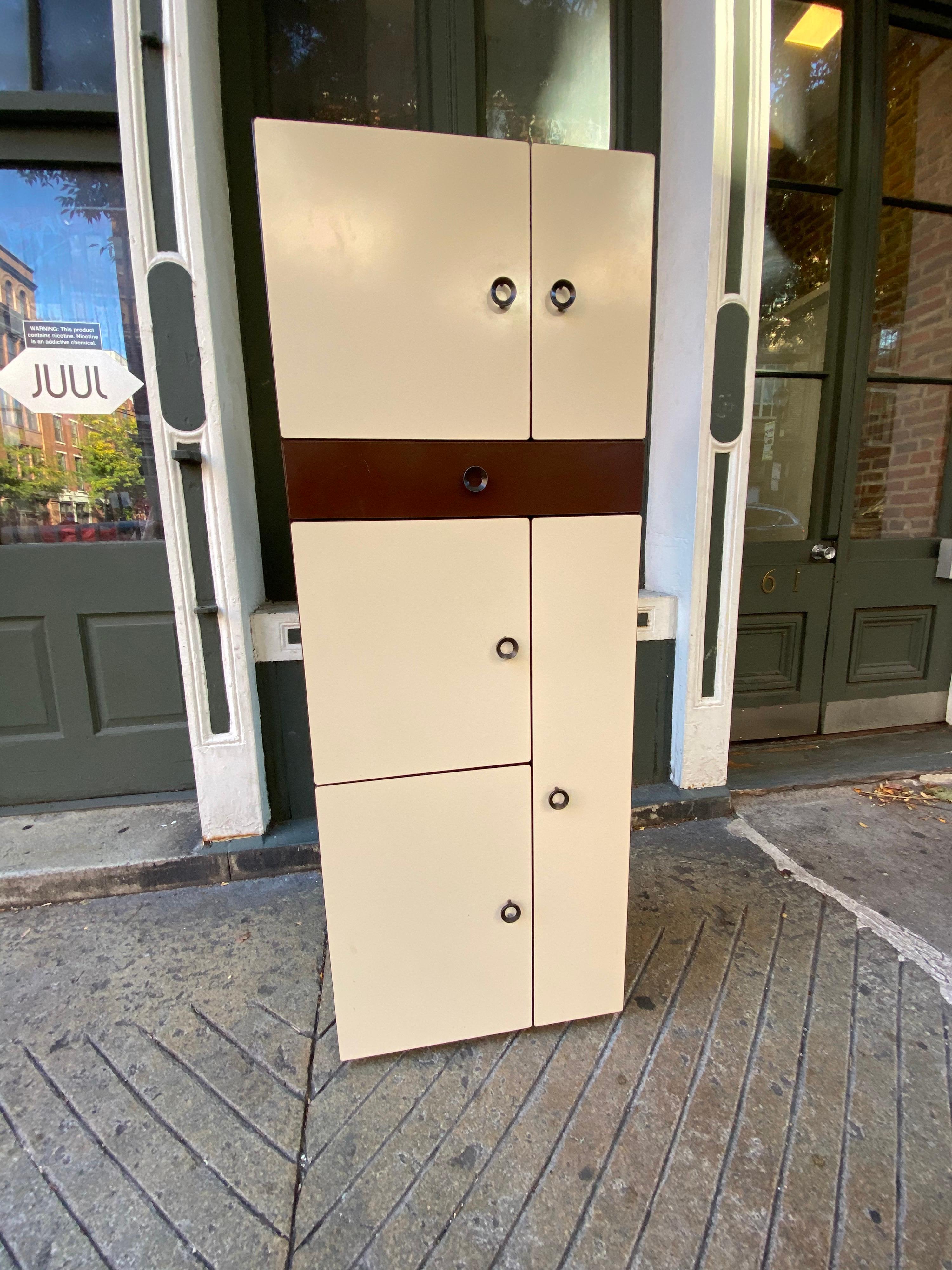 Shallow cabinet with both small chrome feet and hooks to hang from wall. Possibly German or Italian by Design. Unique door design opens to reveal the other half of a shelf! Formica like surface with rubber ends. Overall nice condition and great