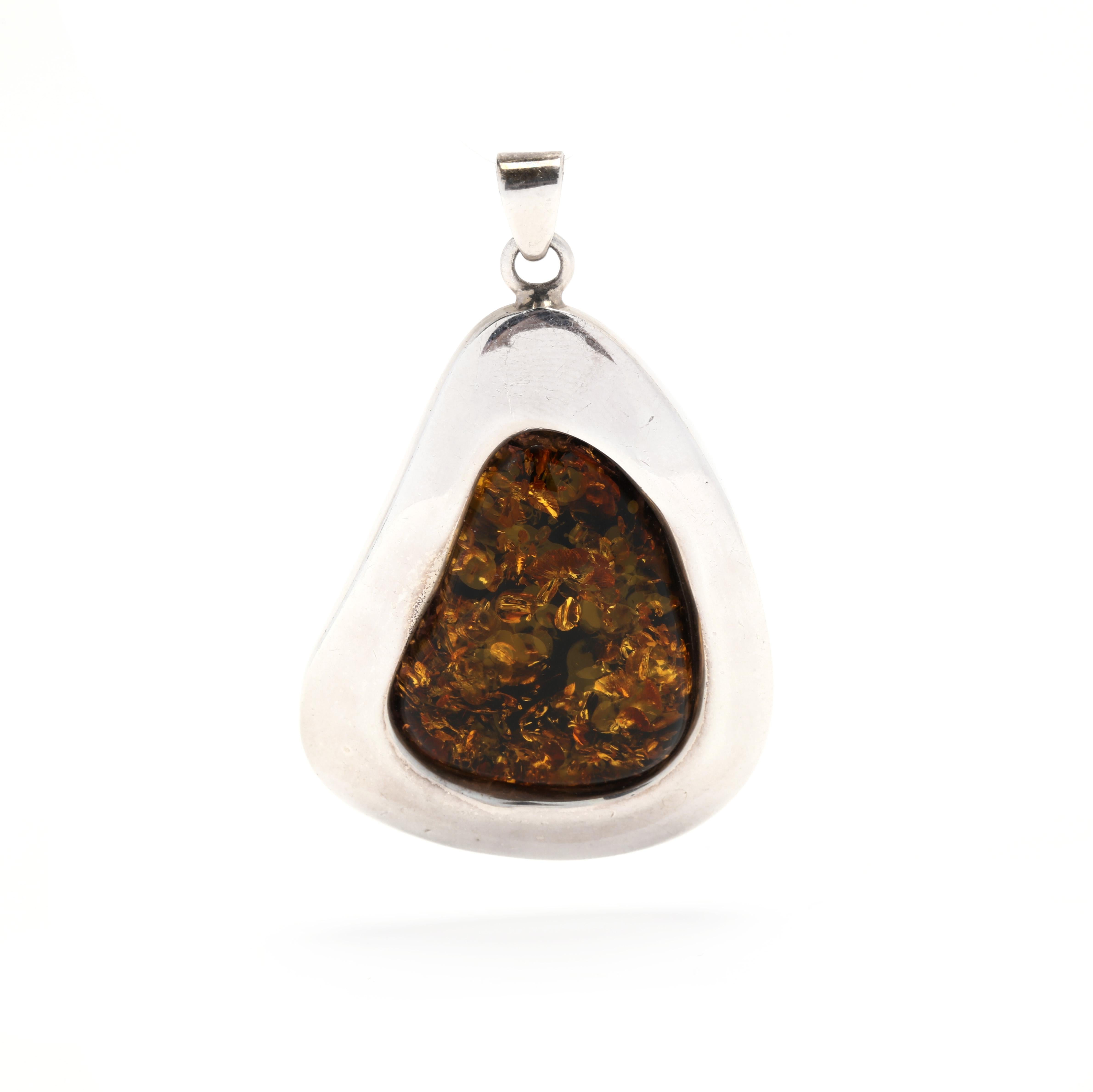 This unique amber pendant is a beautiful and bold statement piece made of sterling silver and freeform amber. Measuring 2 1/4 inches long, it is the perfect accessory to add a touch of elegance to any outfit. The amber gives off a warm, golden glow